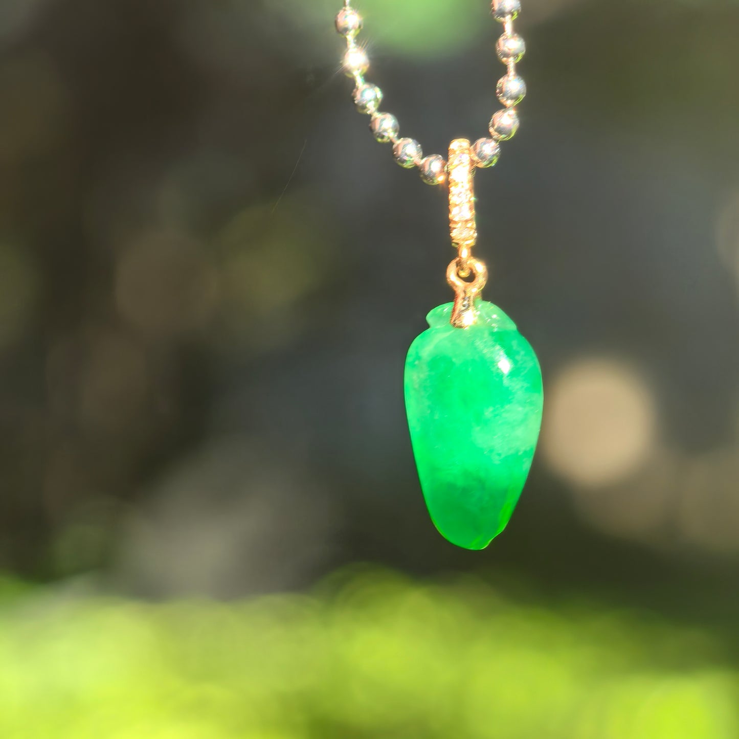 Translucent vivid green jadeite bamboo leaf pendant glowing under natural light.

