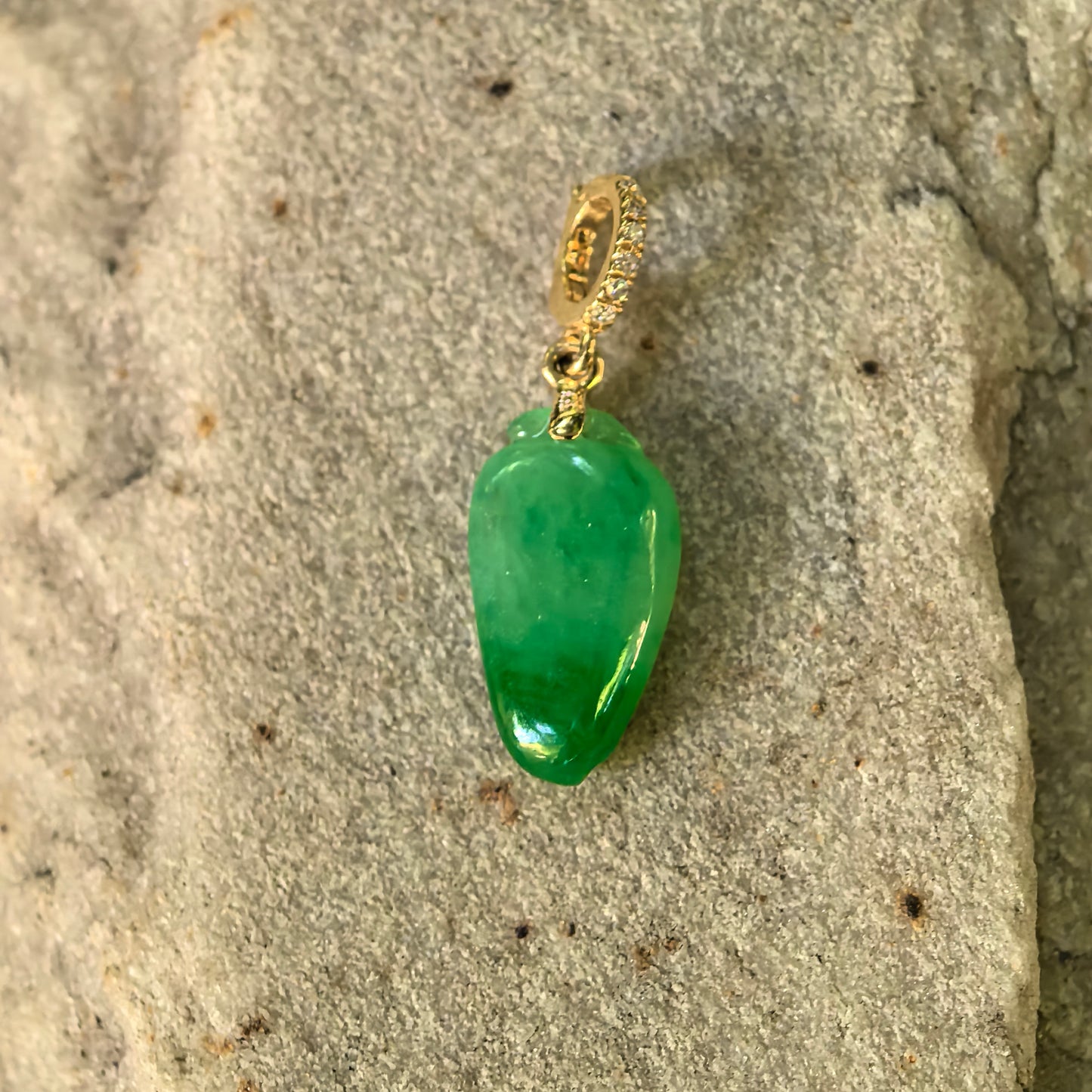 Small carved bamboo leaf jadeite pendant displayed on stone with 18K gold bail.
