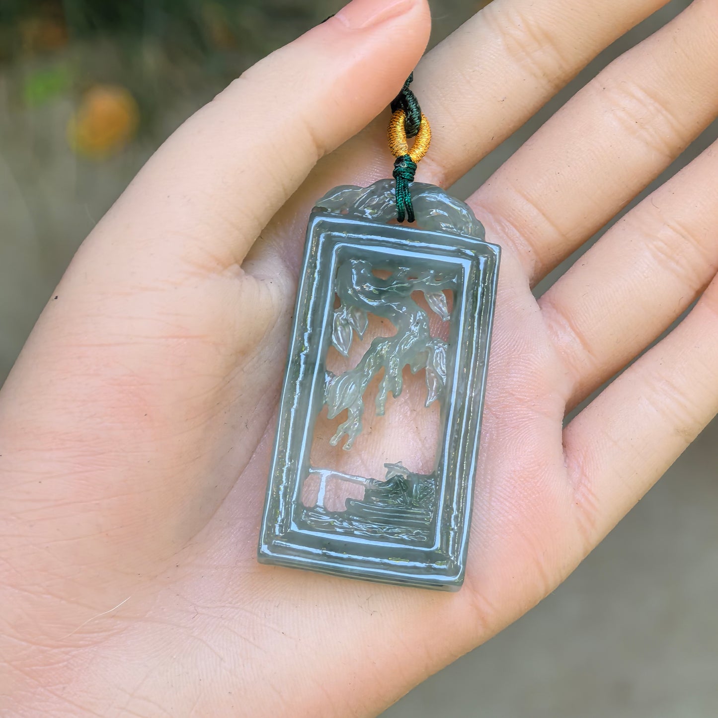 Pale green openwork Solitary Fishing jadeite pendant displayed in hand with rectangular plaque carving.
