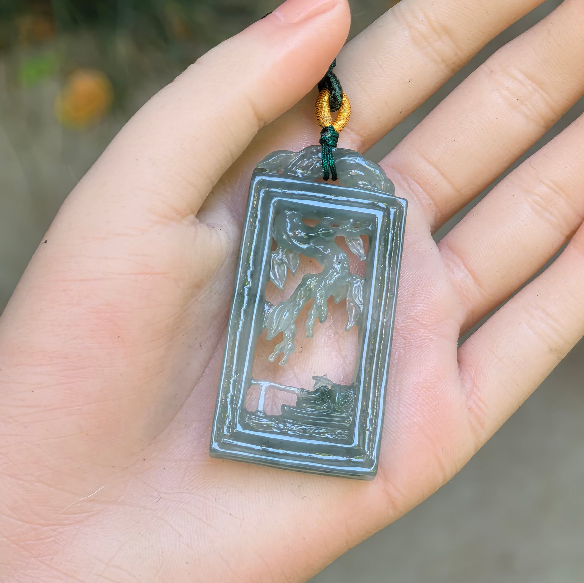 Pale green openwork Solitary Fishing jadeite pendant displayed in hand with rectangular plaque carving.
