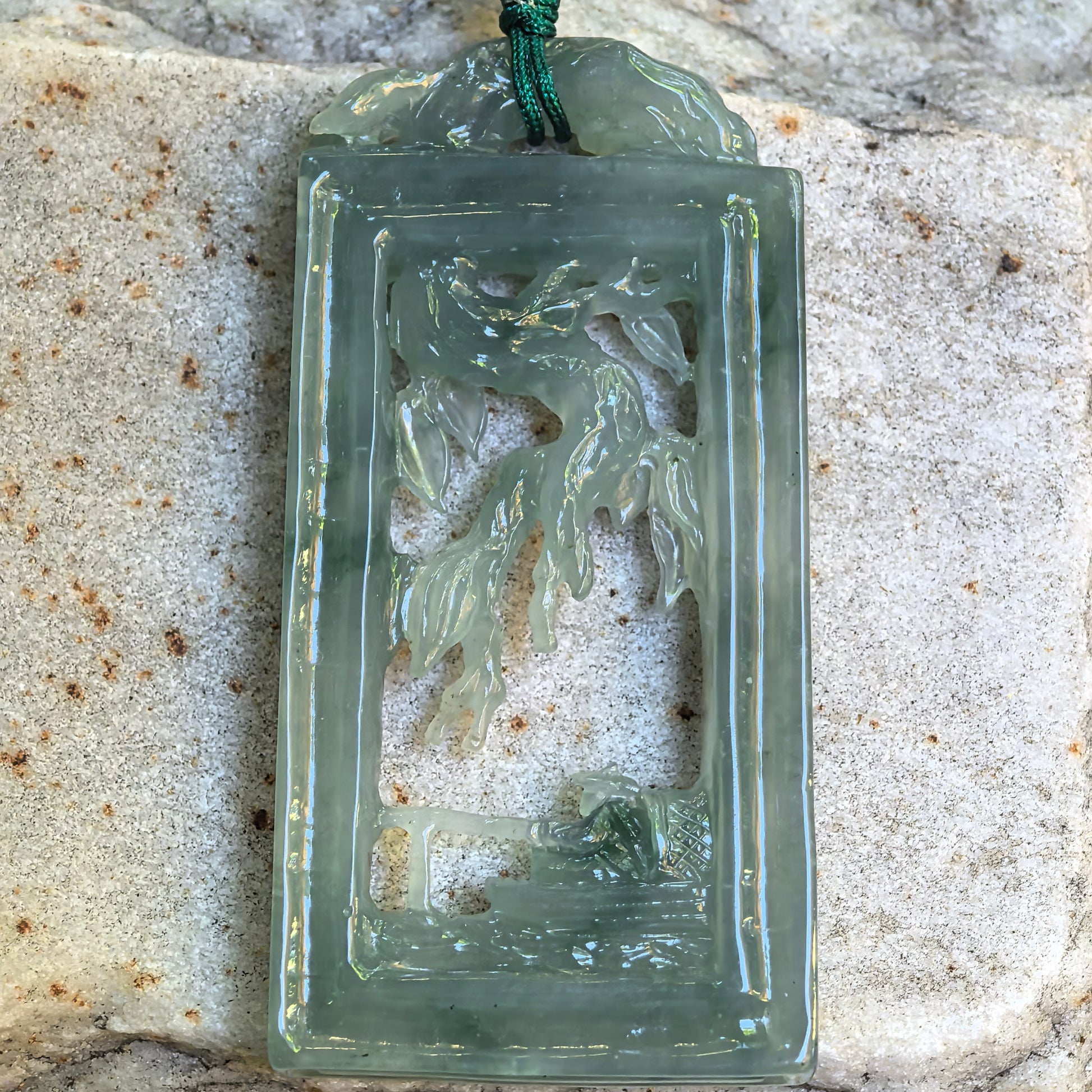 Close-up of icy glutinous pale green jadeite pendant showing hollowed-out fishing landscape details.

