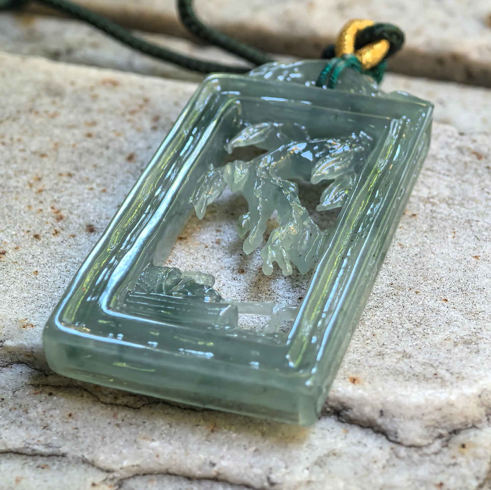 Natural Grade-A pale green carved jadeite plaque pendant on stone surface with openwork scenery.
