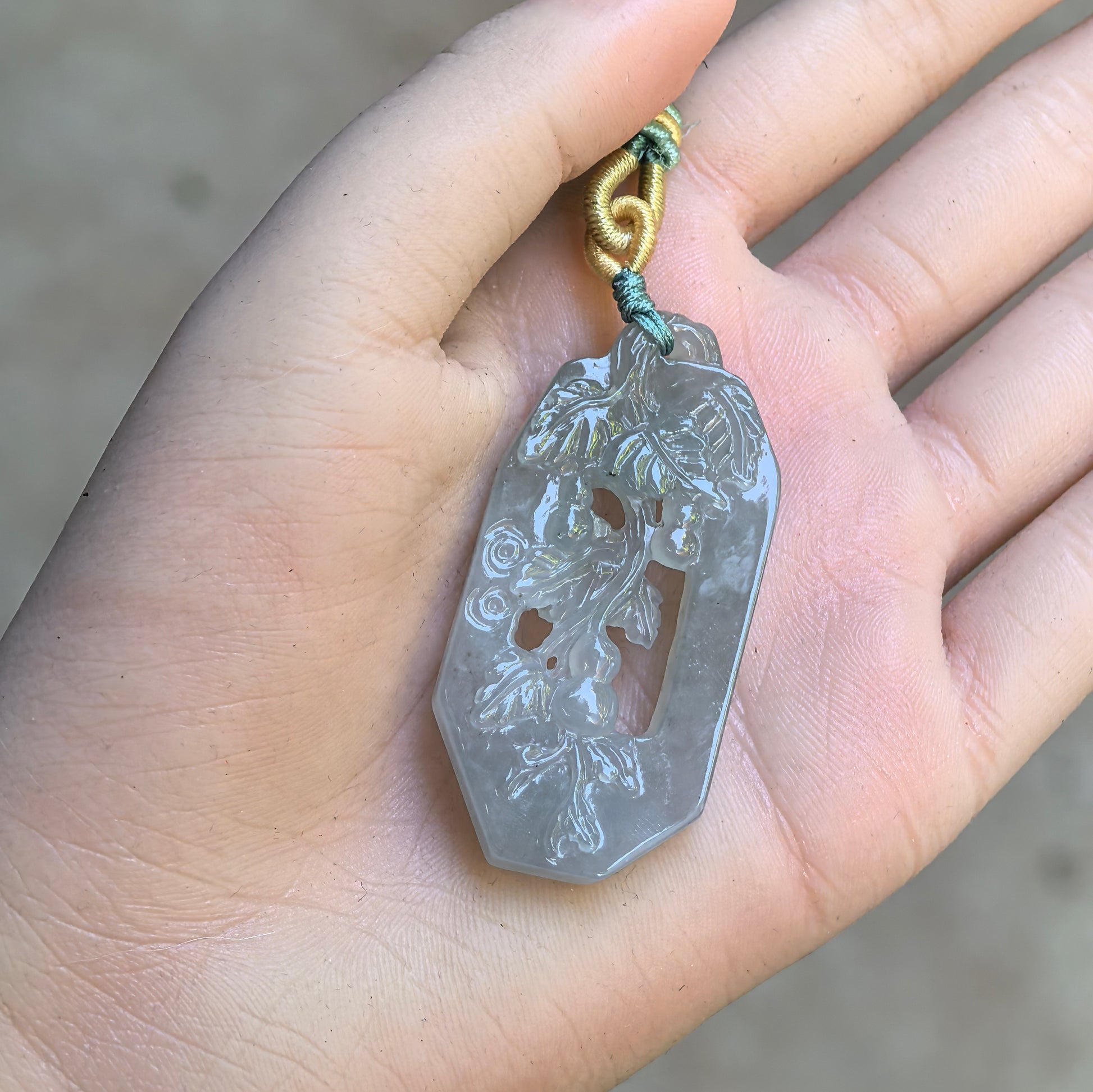 Pale green openwork gourd vine jadeite pendant displayed in hand with carved leaf and vine details.
