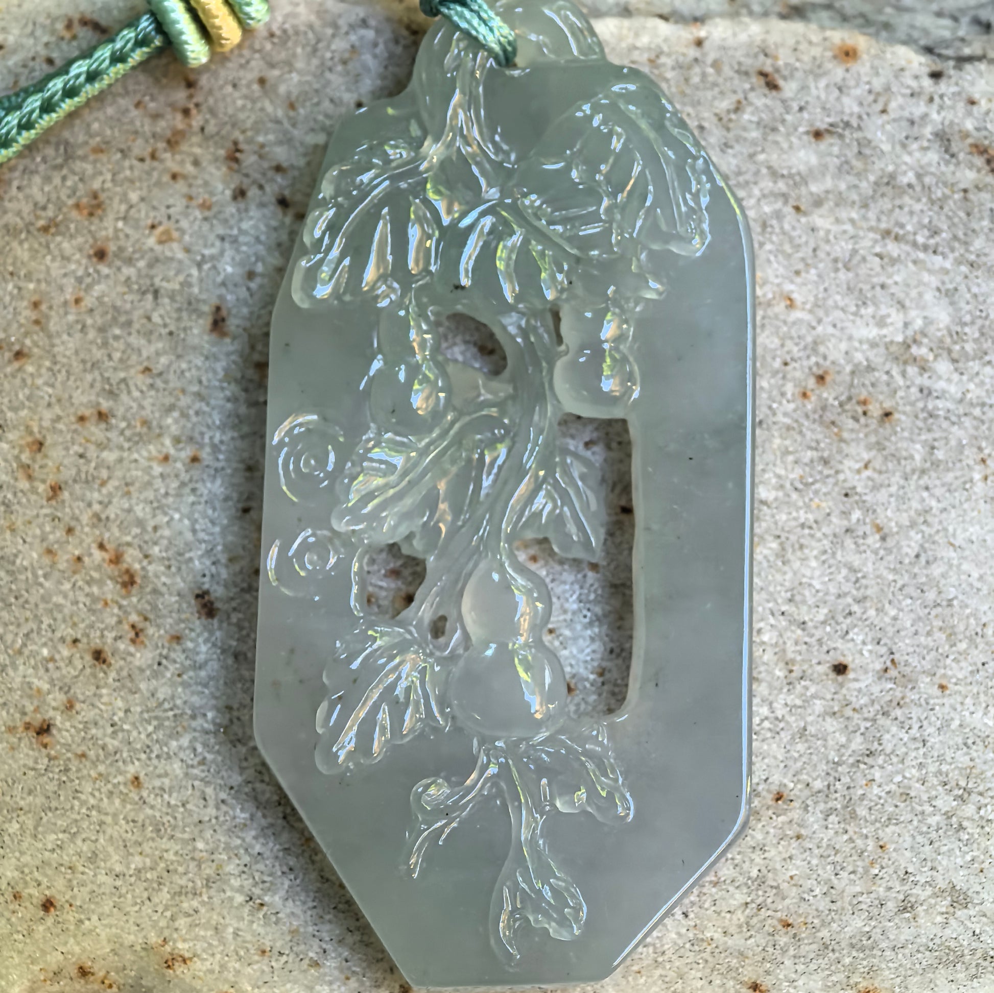 Close-up of icy glutinous pale green jadeite pendant showing hollowed-out gourd vine carving.
