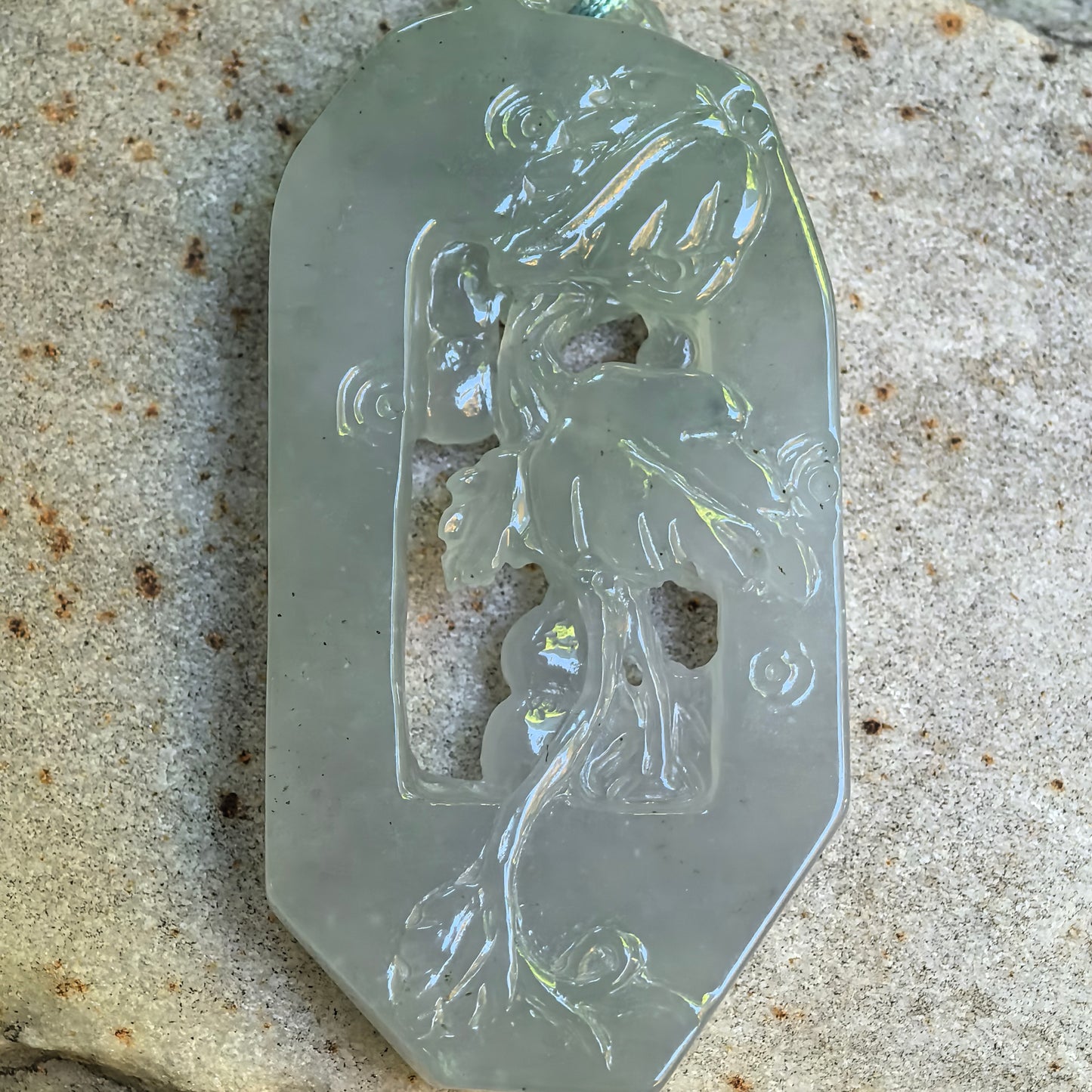 Natural Grade-A pale green carved jadeite pendant on stone surface with openwork vine design.
