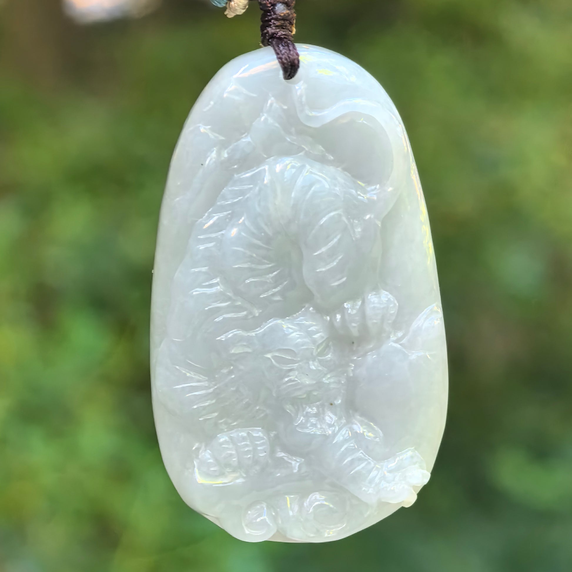 Close-up of milky white pale green tiger jadeite pendant showing detailed relief carving.
