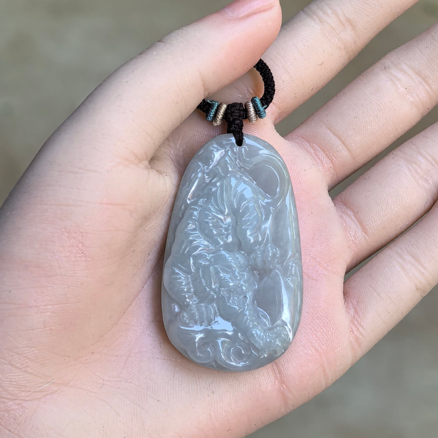 Glutinous pale green carved tiger jadeite pendant displayed in hand with cord.
