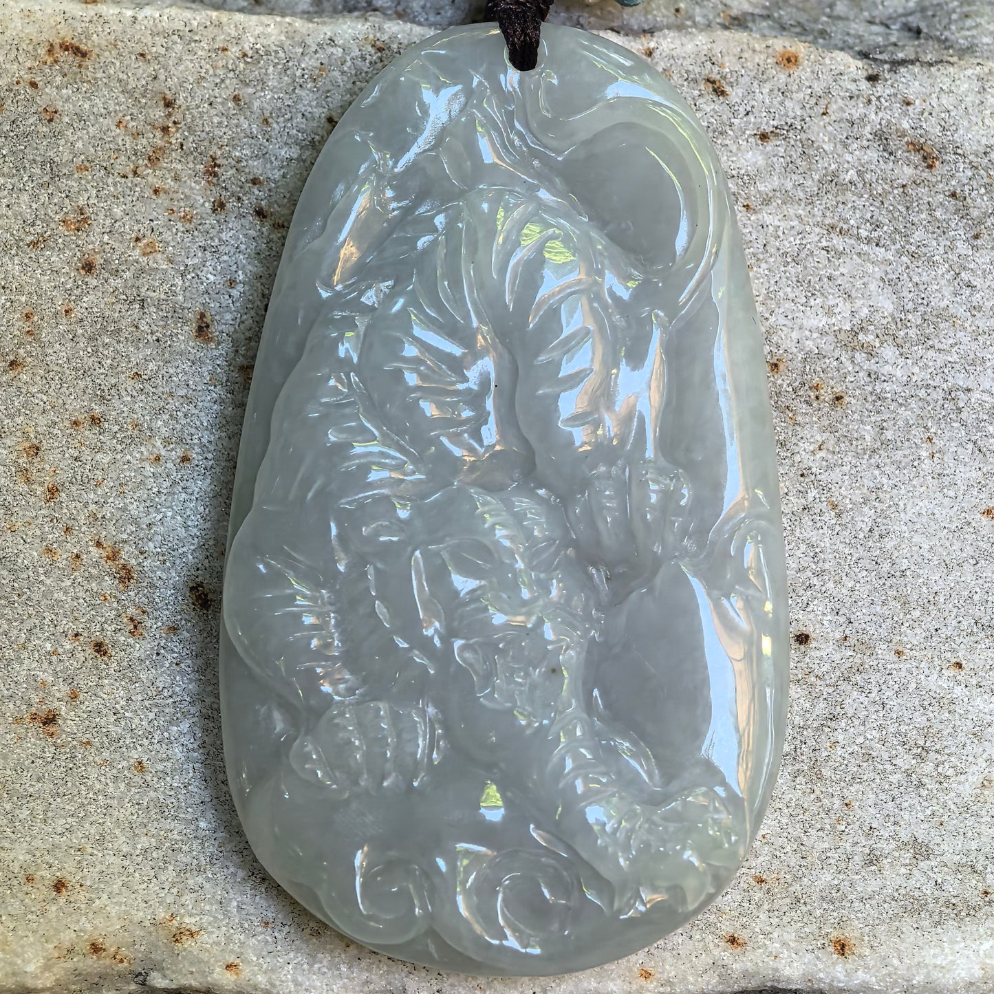 Detailed tiger carved jadeite pendant shown on stone surface with soft translucent texture.
