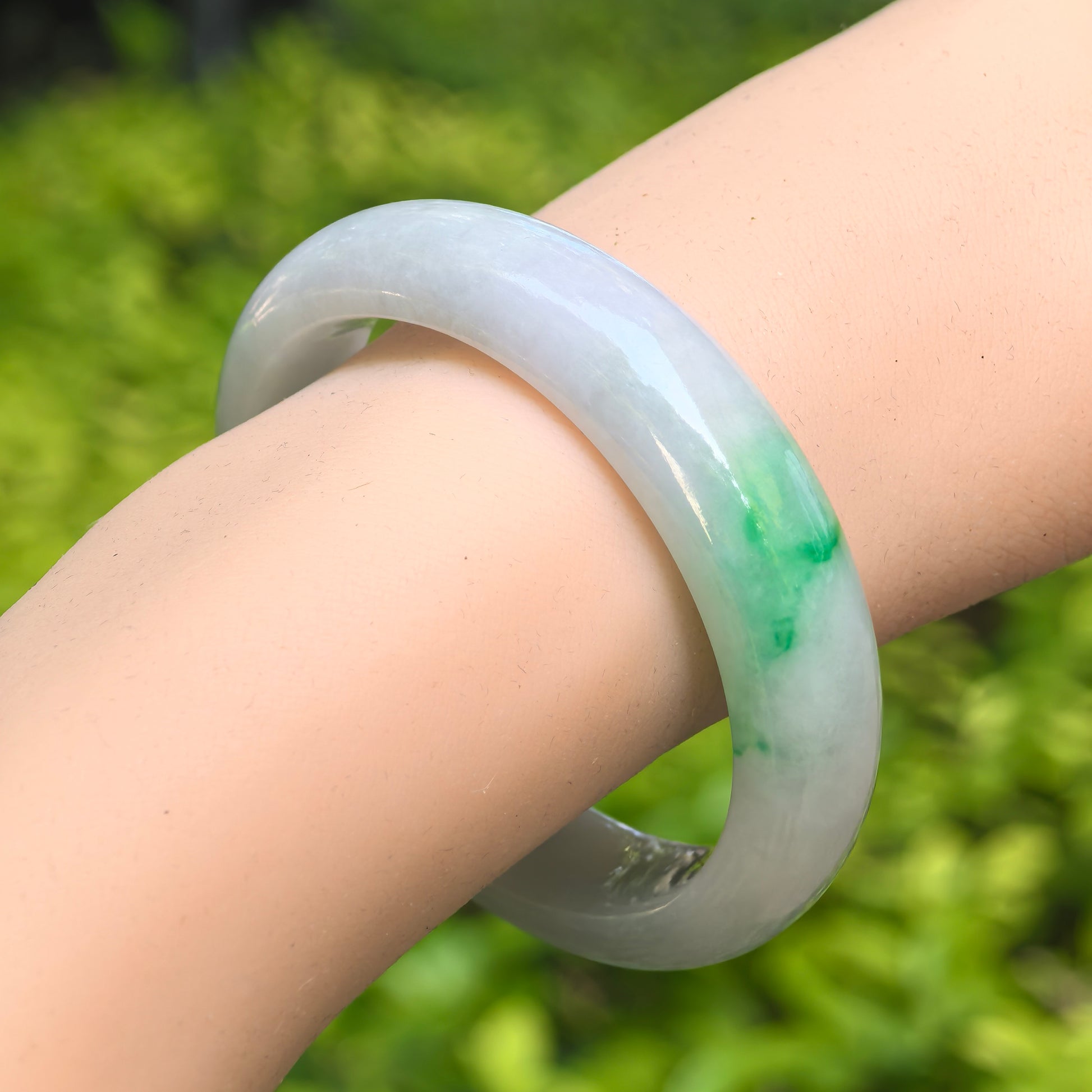 Natural Grade-A glutinous white green oval jadeite bangle worn on the wrist with fresh green accent.
