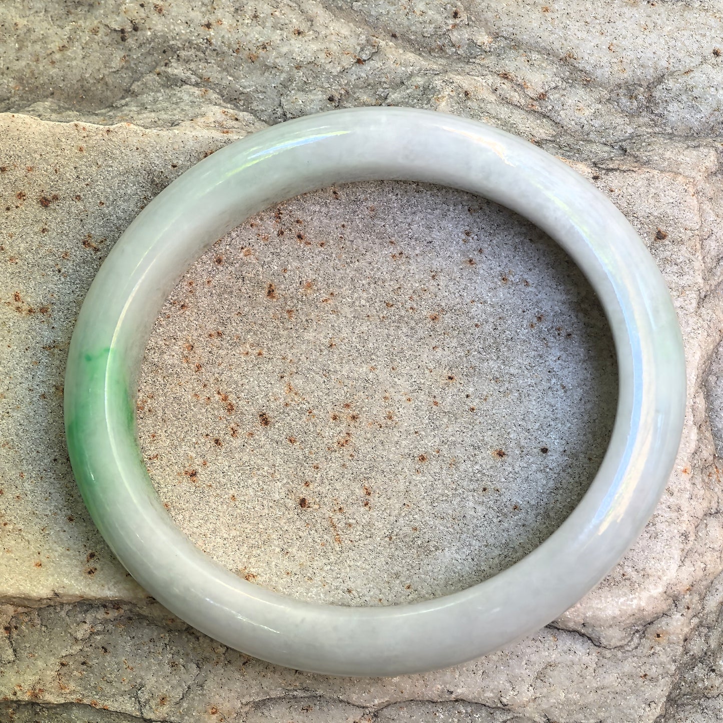 Oval jadeite bangle displayed on stone with soft white base and light green accent.
