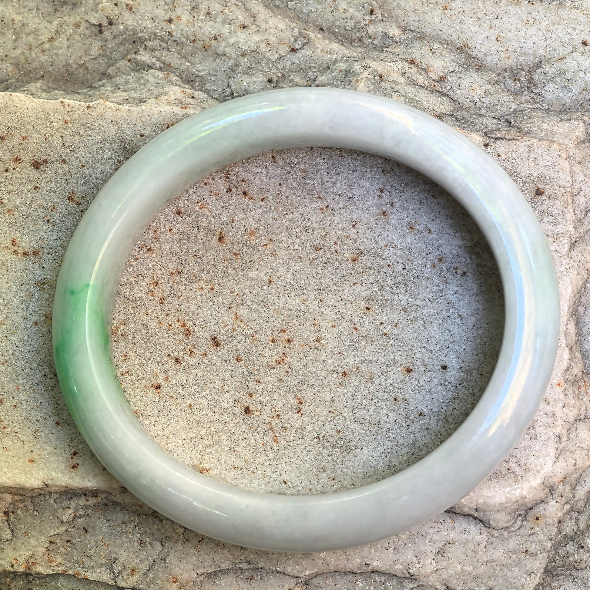 Oval jadeite bangle displayed on stone with soft white base and light green accent.
