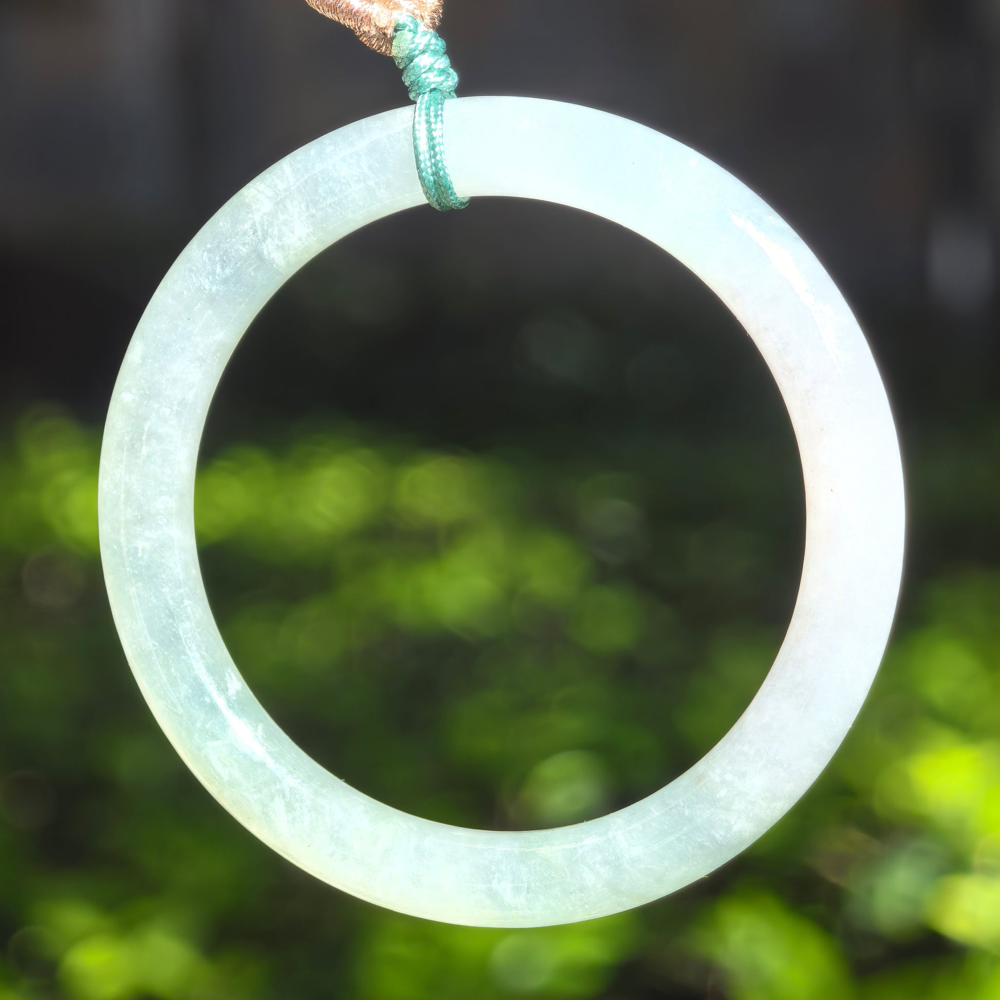 Close-up of light green child jadeite bangle on stone surface showing slim circular form and polished luster.
