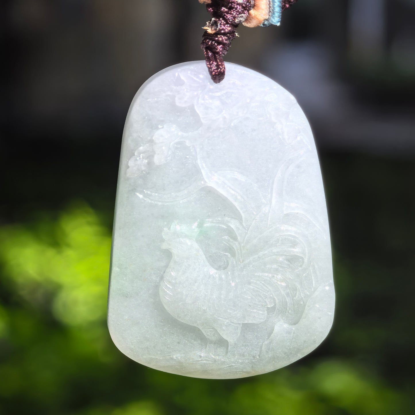 Close-up of light green rooster jadeite pendant showing soft translucency and smooth carved details.
