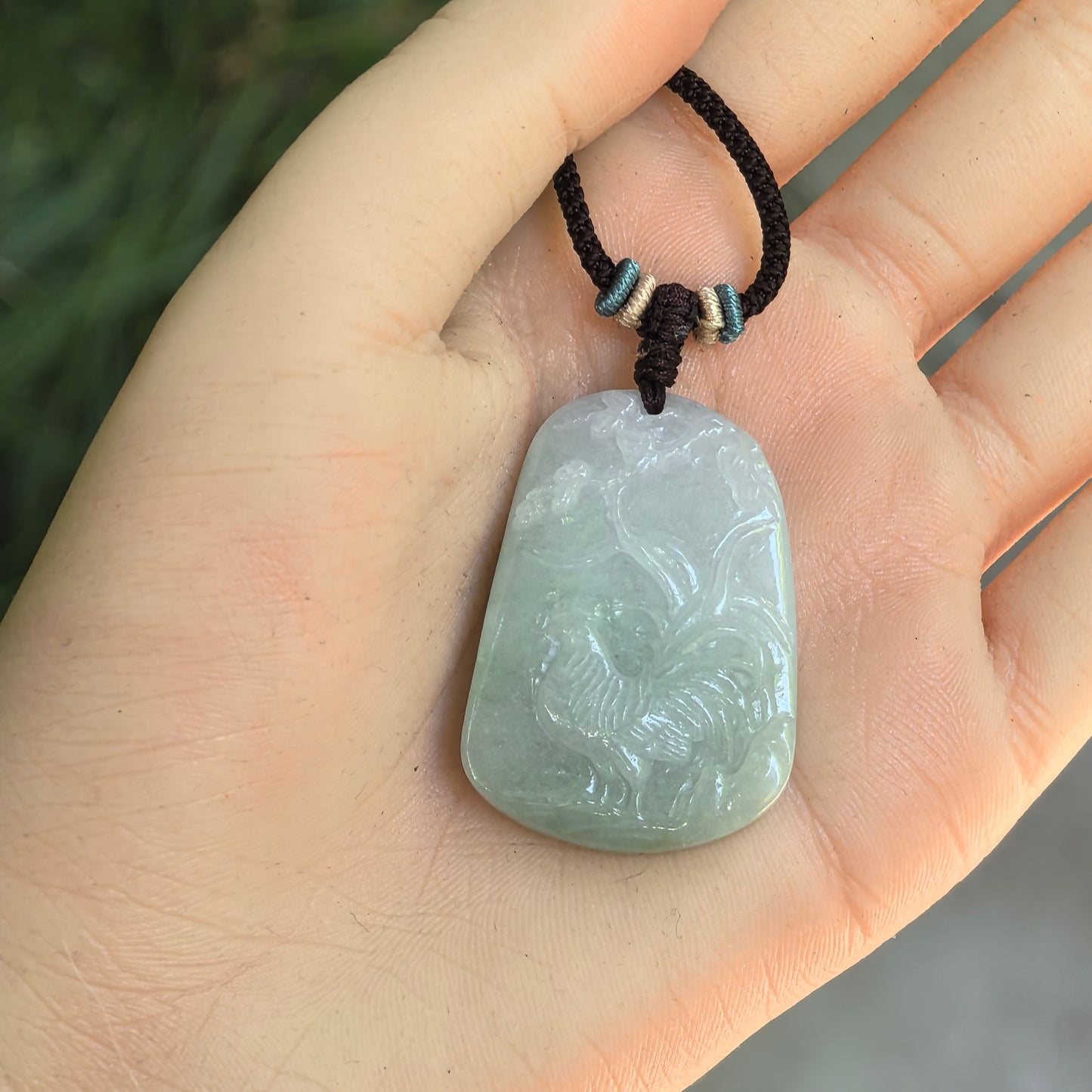 Glutinous light green jadeite rooster pendant displayed in hand with rounded plaque-like shape.
