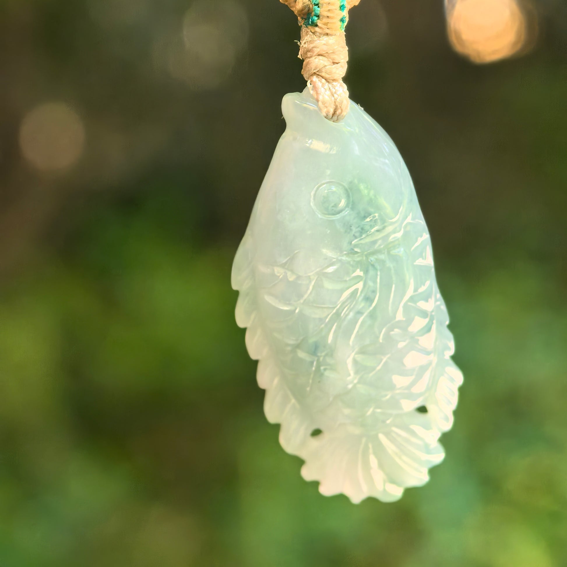 Natural Grade-A glutinous light green fish jadeite pendant hanging on cord with detailed scale and tail carving.
