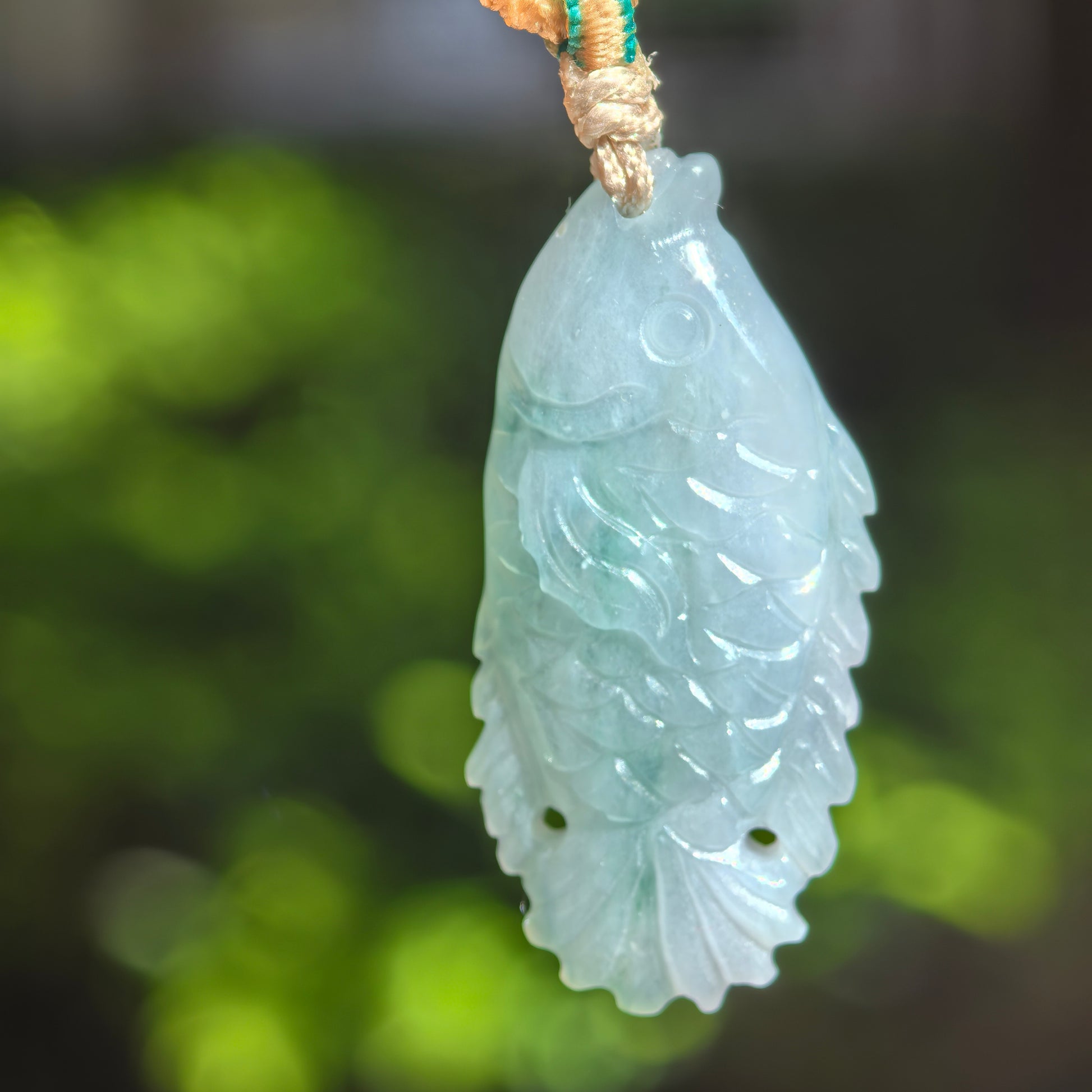 Close-up of light green fish jadeite pendant showing smooth carving, round eye detail, and soft translucency.
