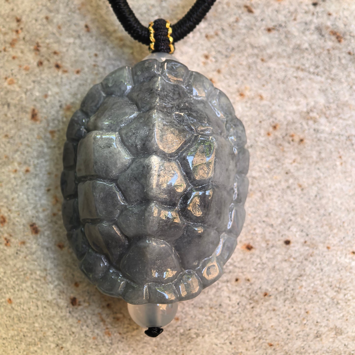 Natural Grade-A gray-black turtle shell jadeite pendant shown on stone surface with detailed raised carving.
