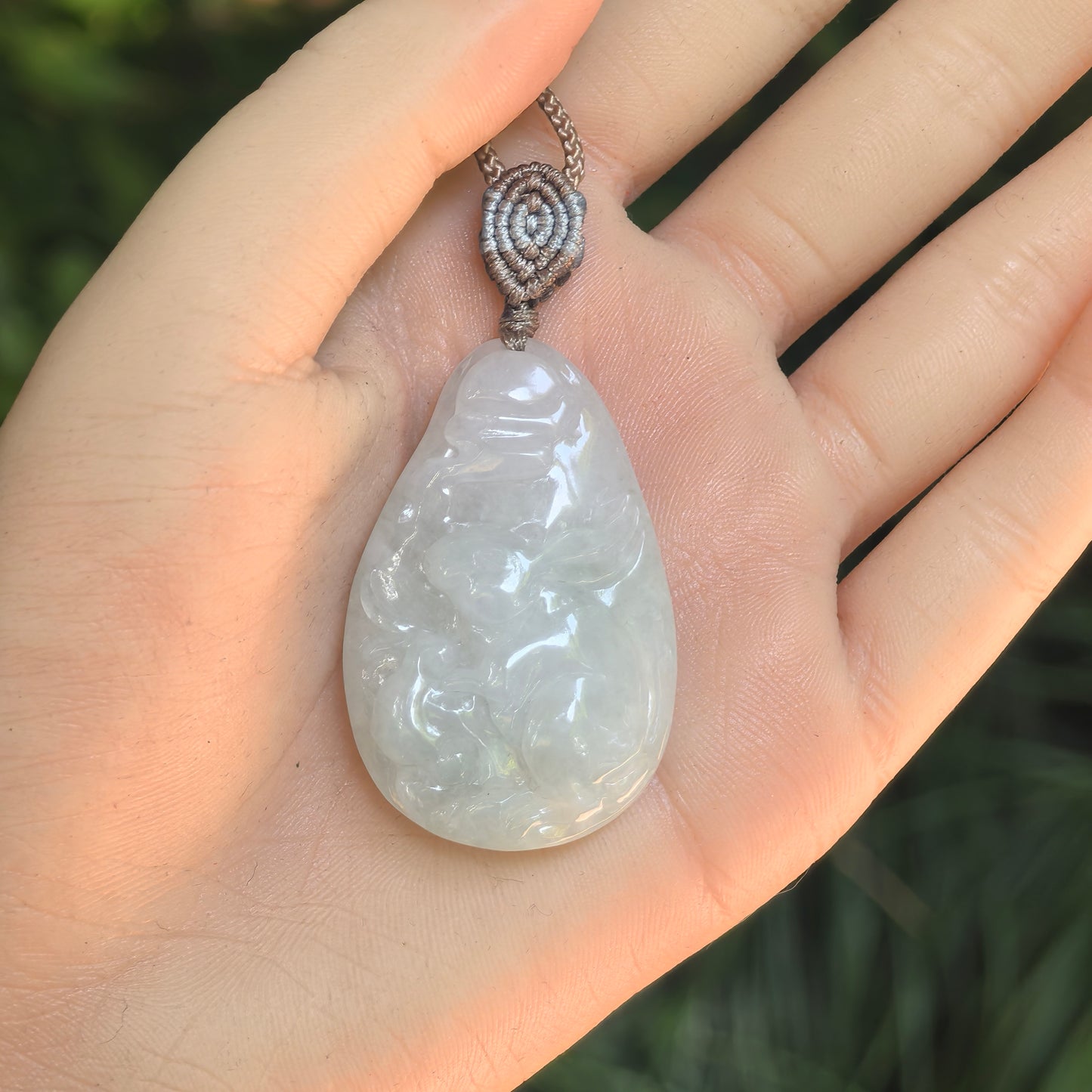 White rabbit jadeite pendant shown on hand, featuring rounded teardrop shape and raised carving.
