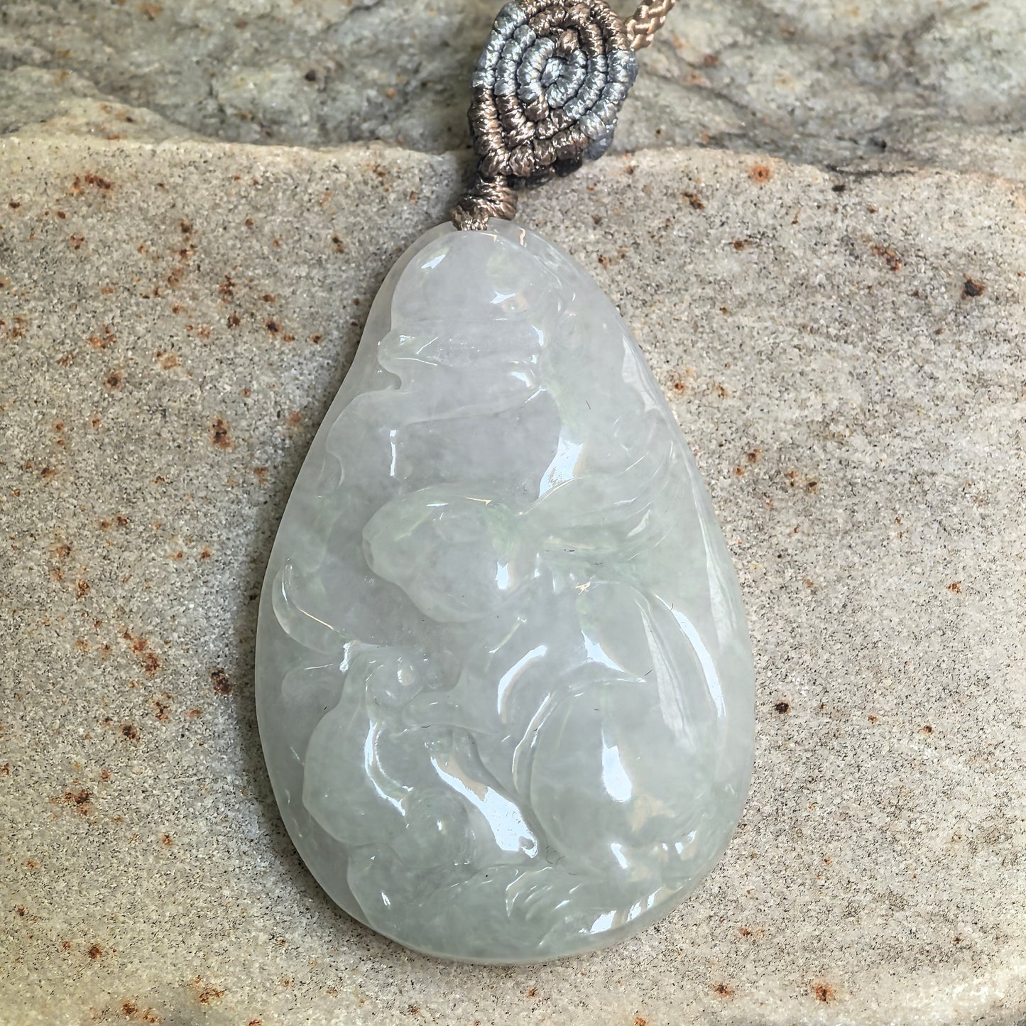 Natural Grade-A white rabbit jadeite pendant displayed on stone with gentle translucency.
