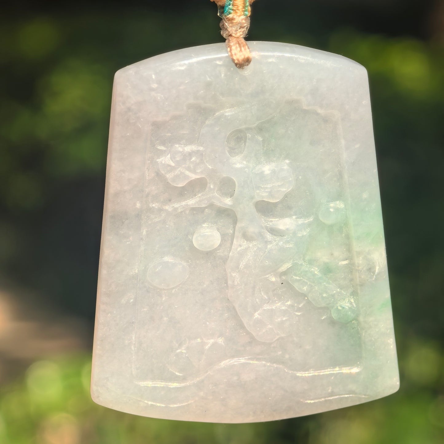 Close-up of white-base jadeite pendant with a soft green accent and raised floral carving.
