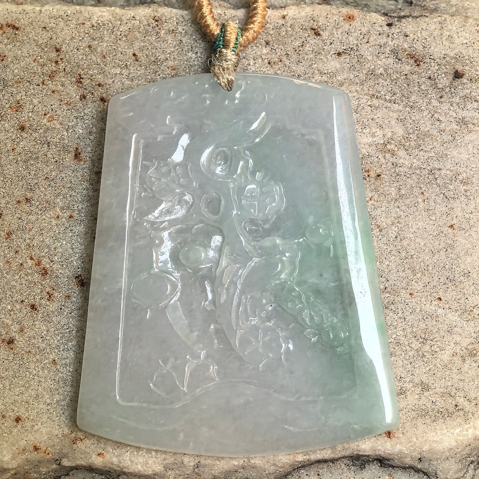 Natural Grade-A floral carved jadeite pendant displayed on stone with soft translucency.
