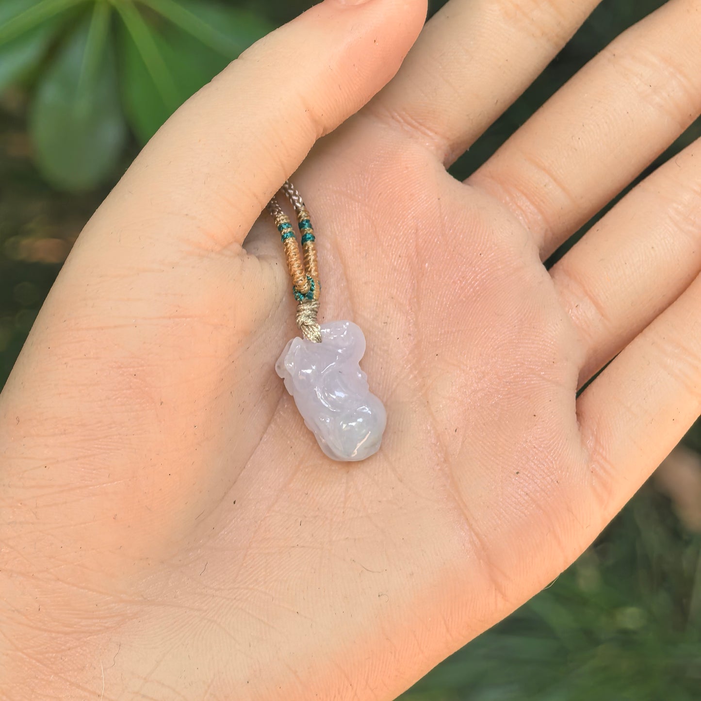 Small white-lavender Tang Horse jadeite pendant displayed in hand with compact rounded carving.
