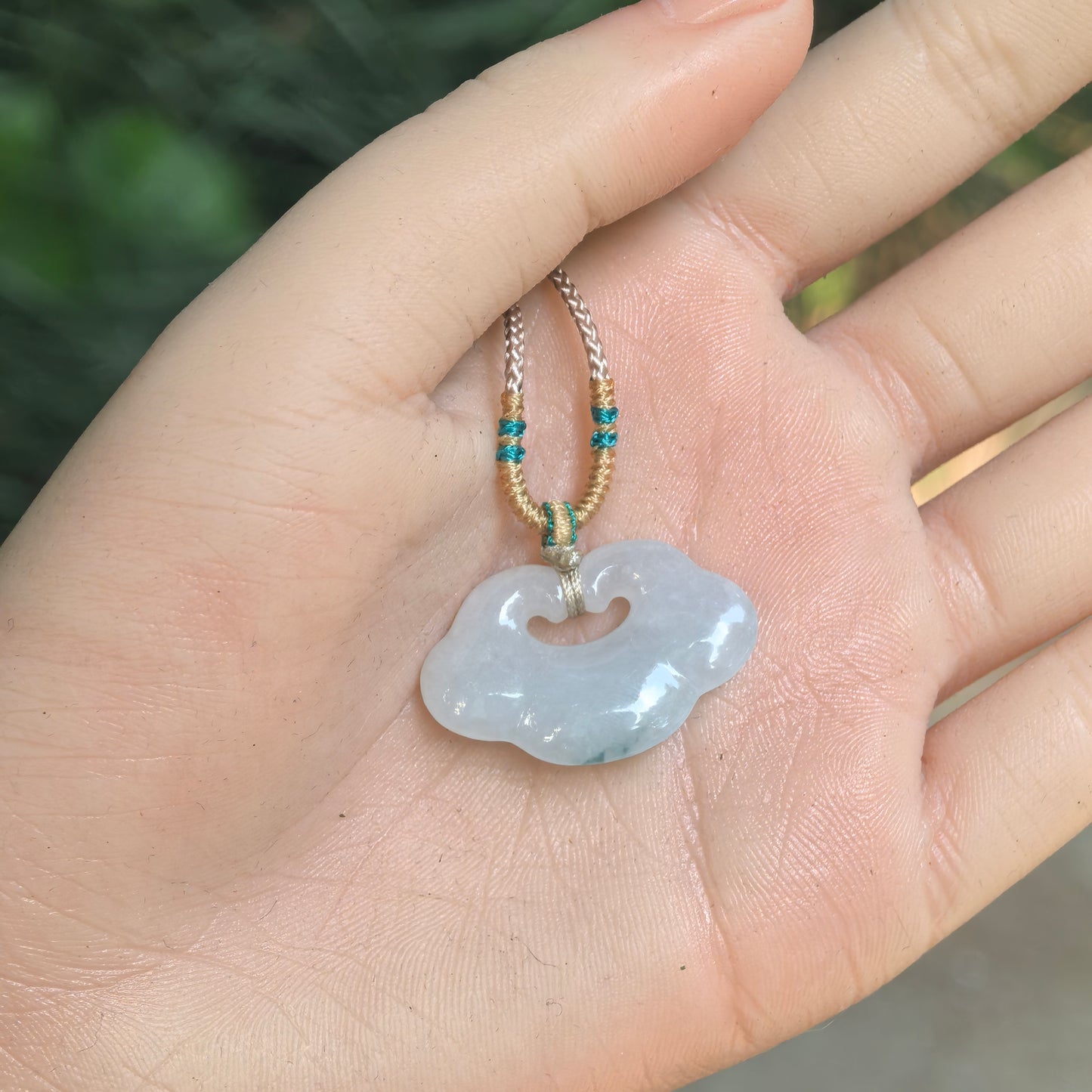 Natural Grade-A white-base jadeite auspicious cloud pendant displayed on hand with cord.