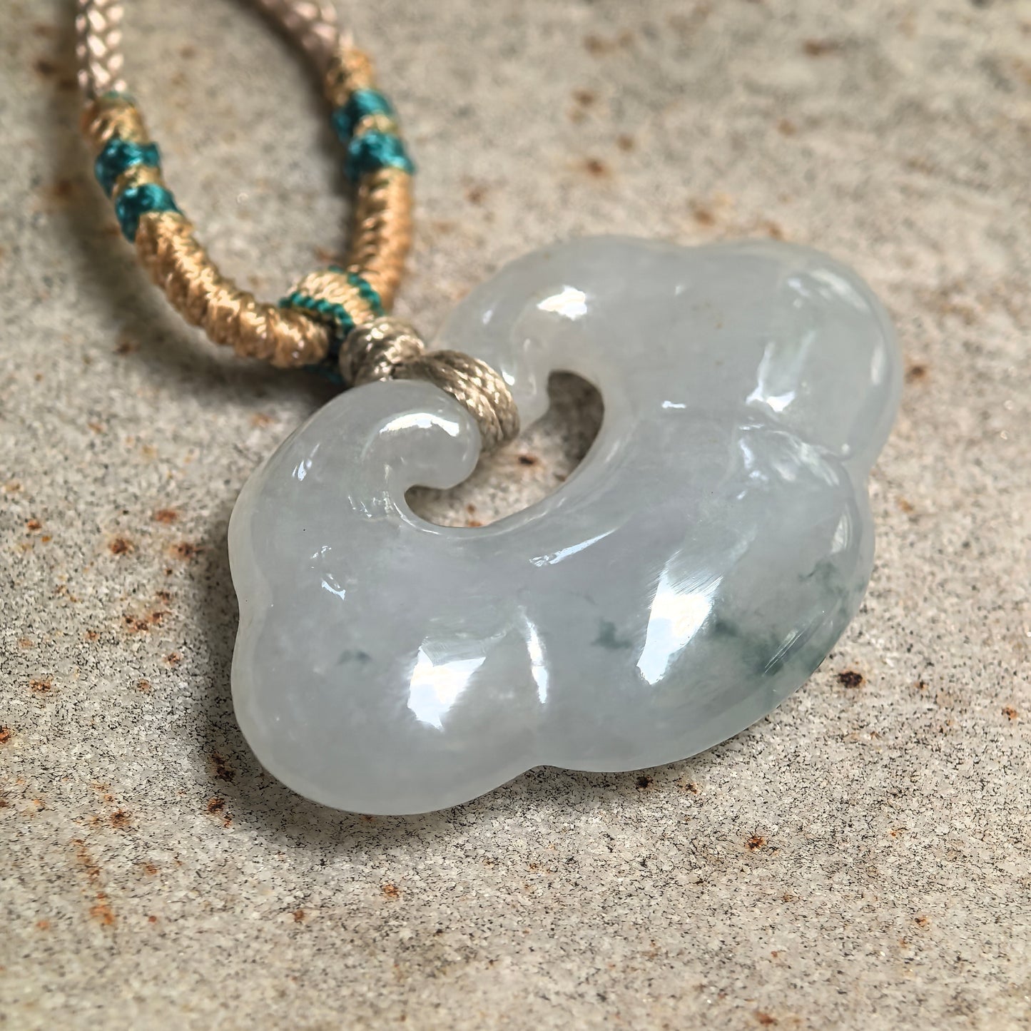 Close-up of white-base glutinous jadeite cloud pendant showing rounded carving and soft light green tones.