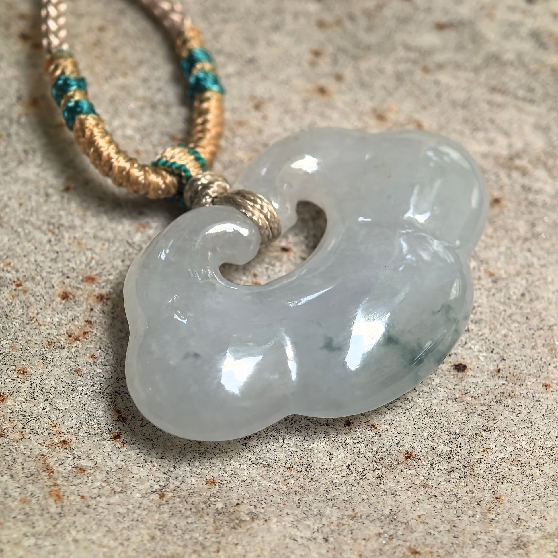 Close-up of white-base glutinous jadeite cloud pendant showing rounded carving and soft light green tones.