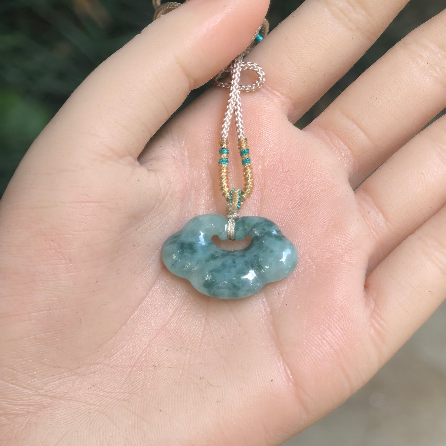 Light green jadeite auspicious cloud pendant displayed in hand with attached cord.
