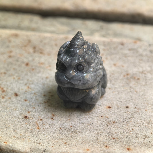 Natural Grade-A glutinous black-gray cute Pixiu jadeite ornament shown from the front on stone.
