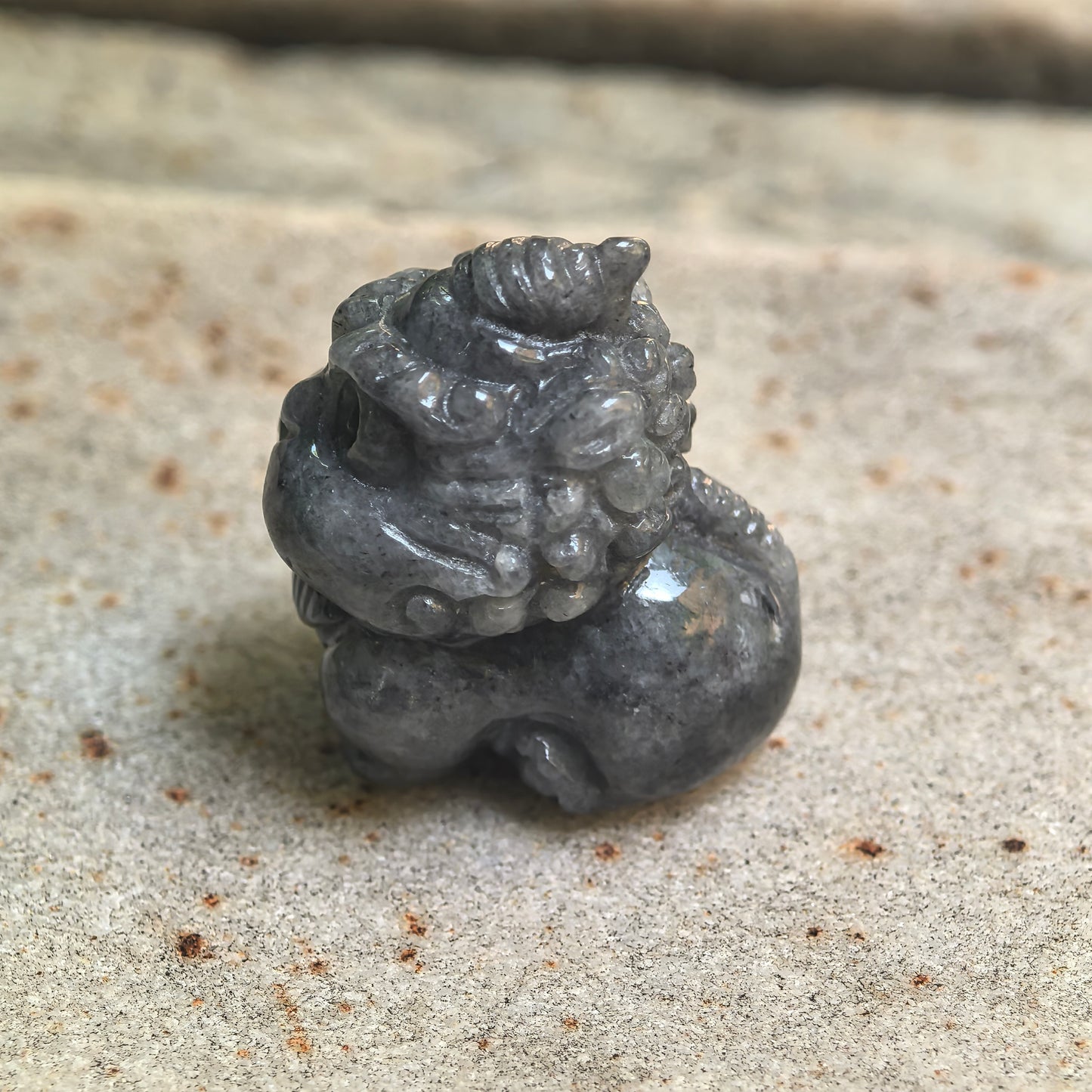 Side view of glutinous black-gray Pixiu jadeite ornament showing carved horn and rounded body.
