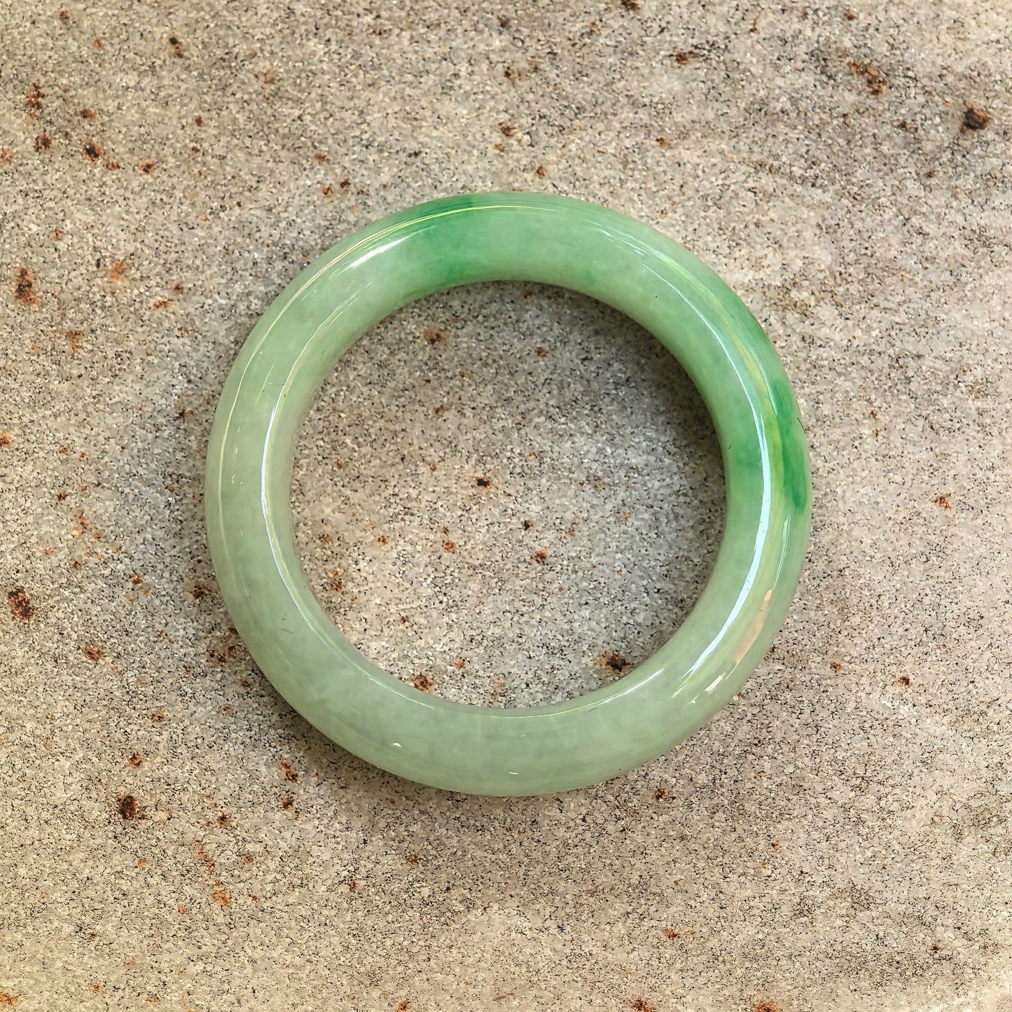 Glutinous light green jadeite ring band displayed on stone background.

