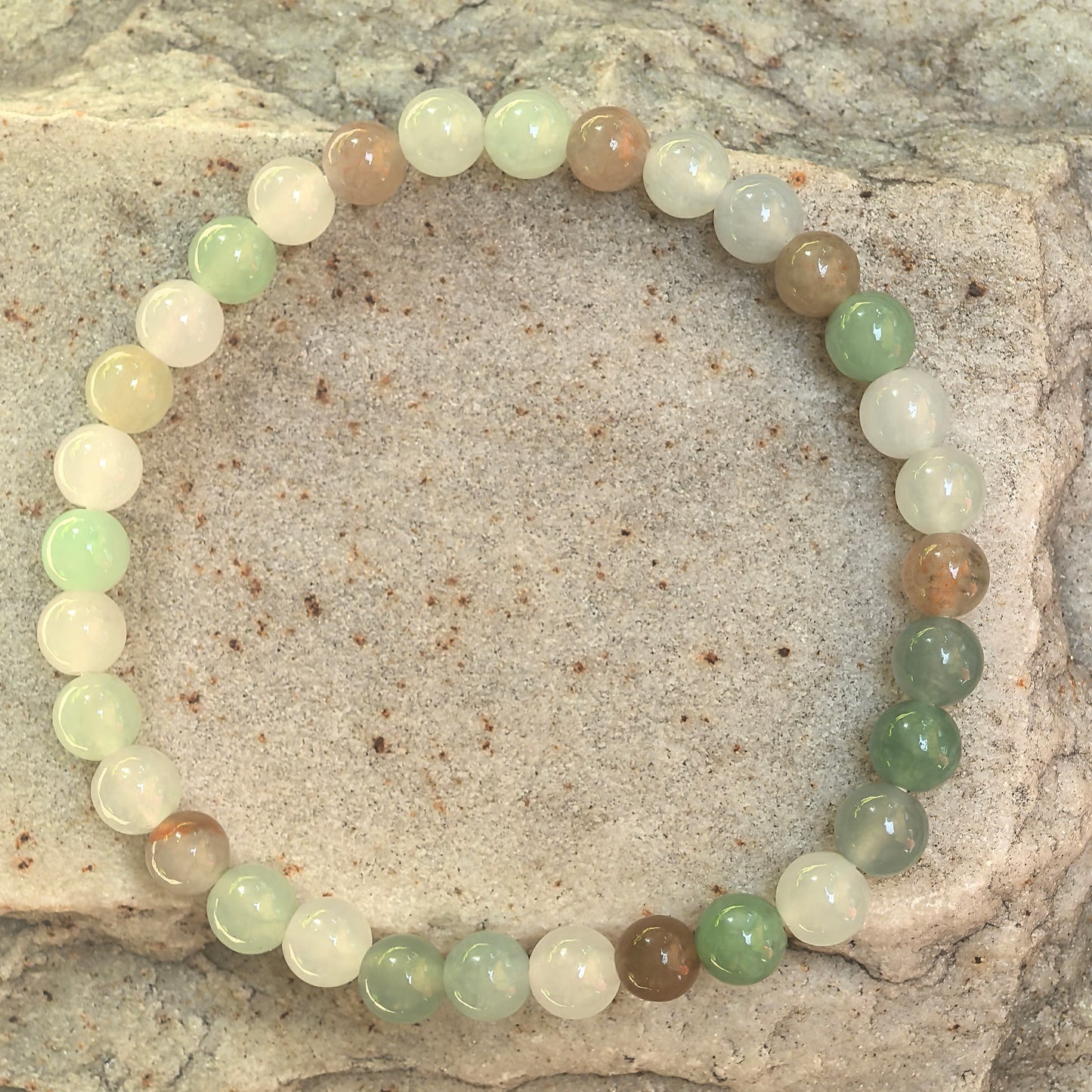 Natural jadeite beaded bracelet displayed on outdoor stone background.
