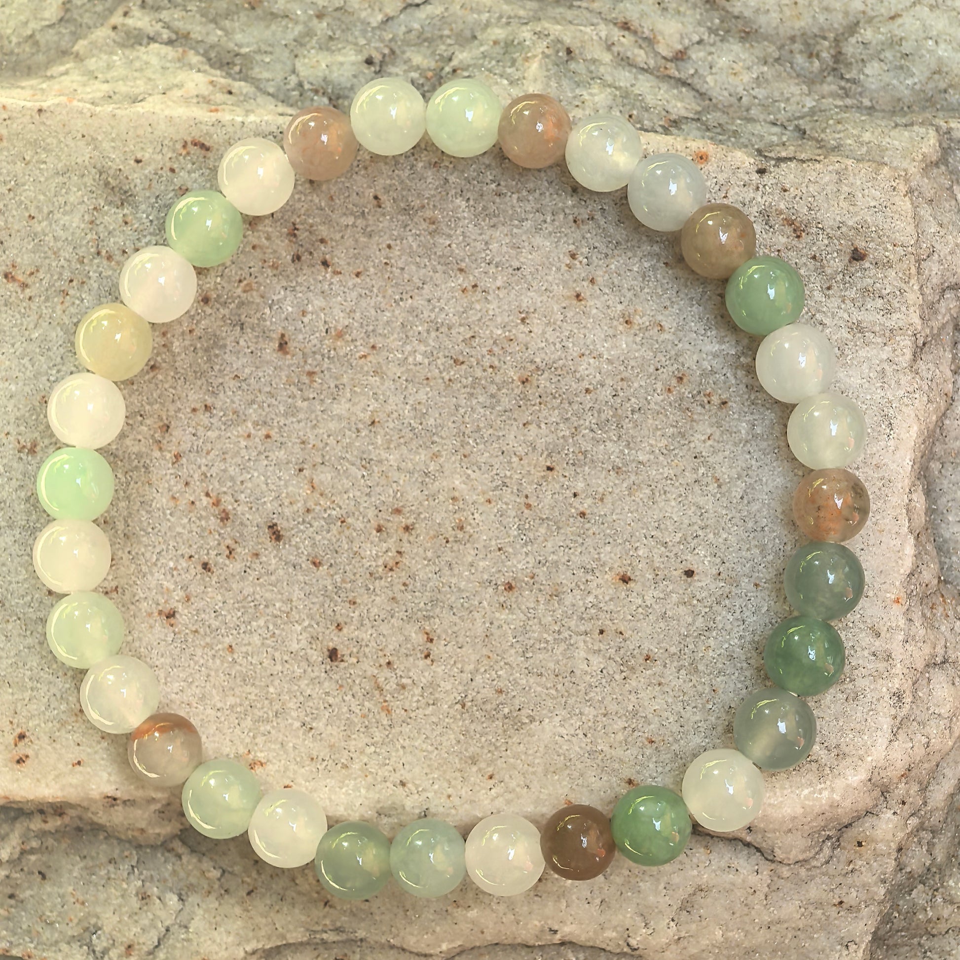 Natural jadeite beaded bracelet displayed on outdoor stone background.
