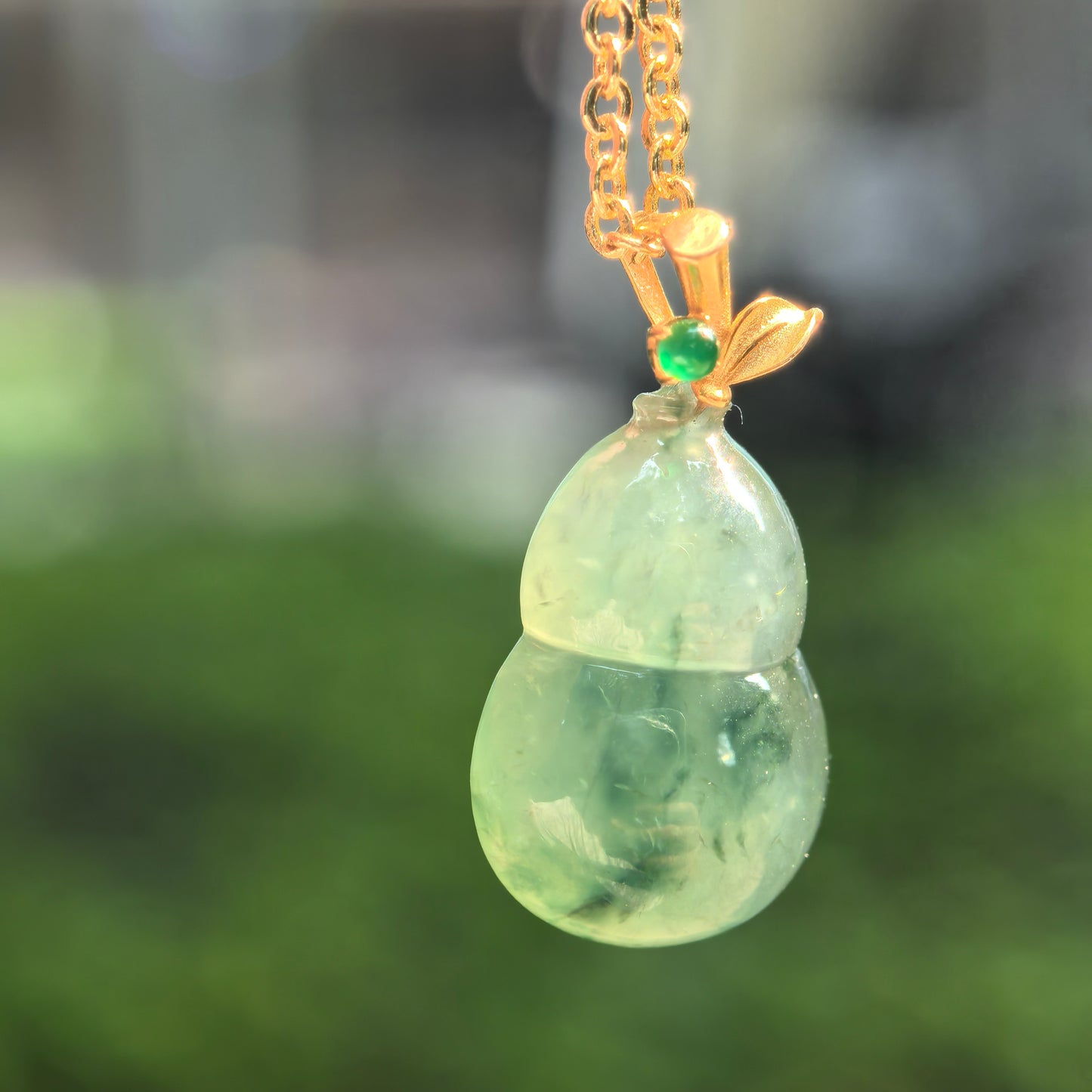 Close-up of small green jadeite gourd pendant showing deep floating flower pattern and glossy texture.
