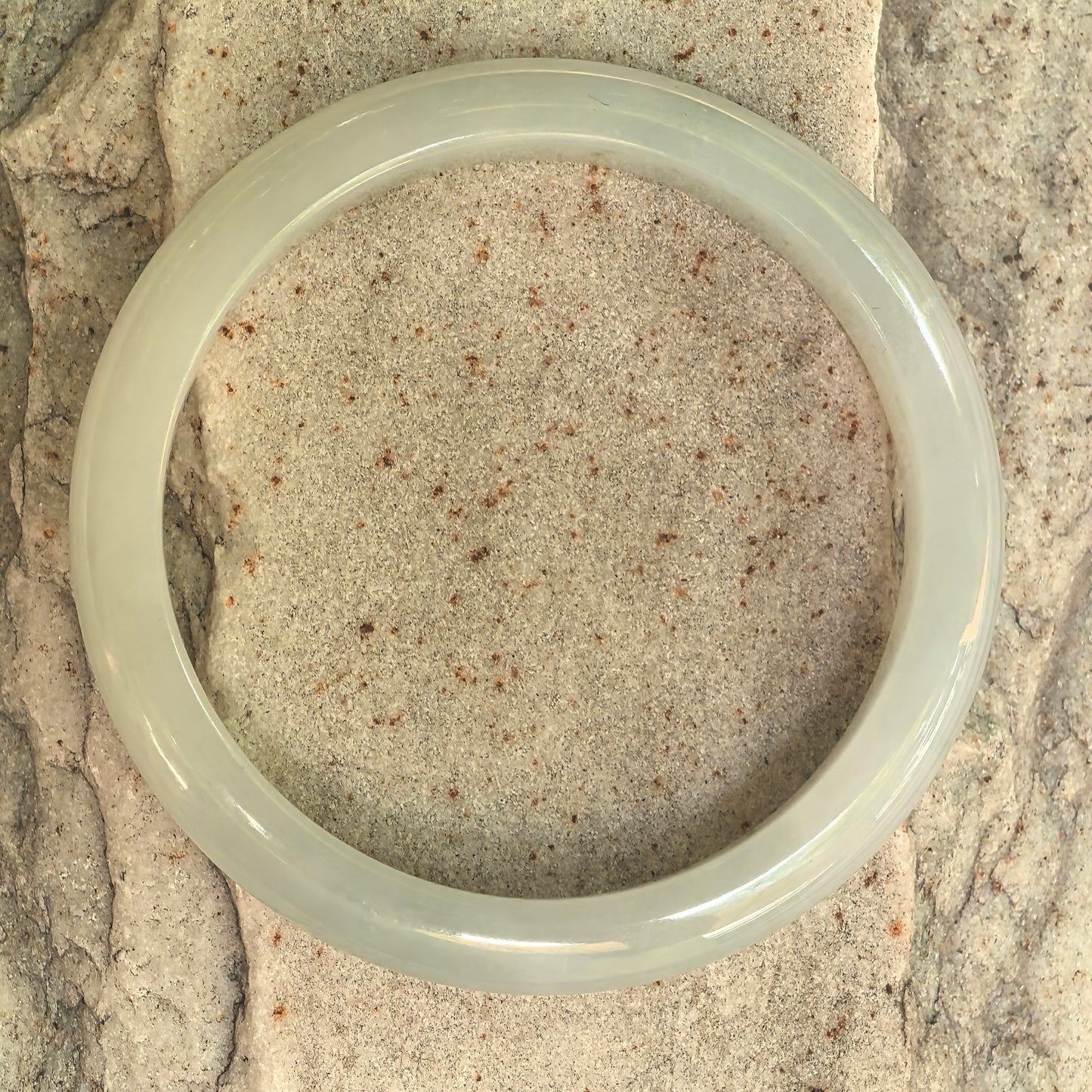 Natural Grade-A white-base light green D-shape jadeite bangle displayed flat on stone.
