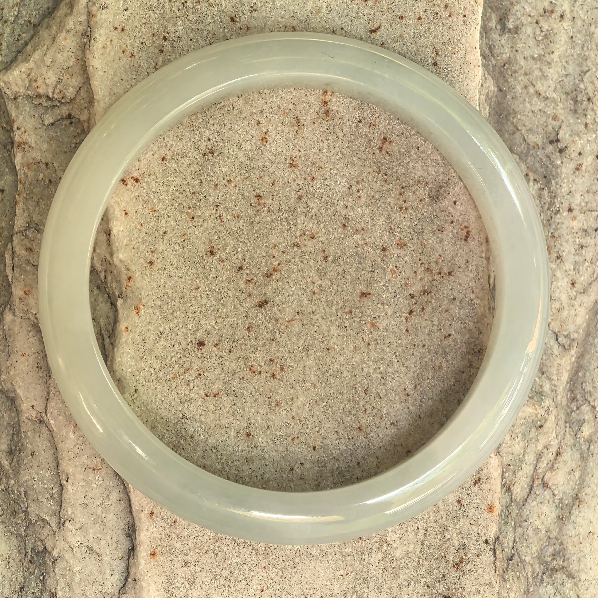 Natural Grade-A white-base light green D-shape jadeite bangle displayed flat on stone.
