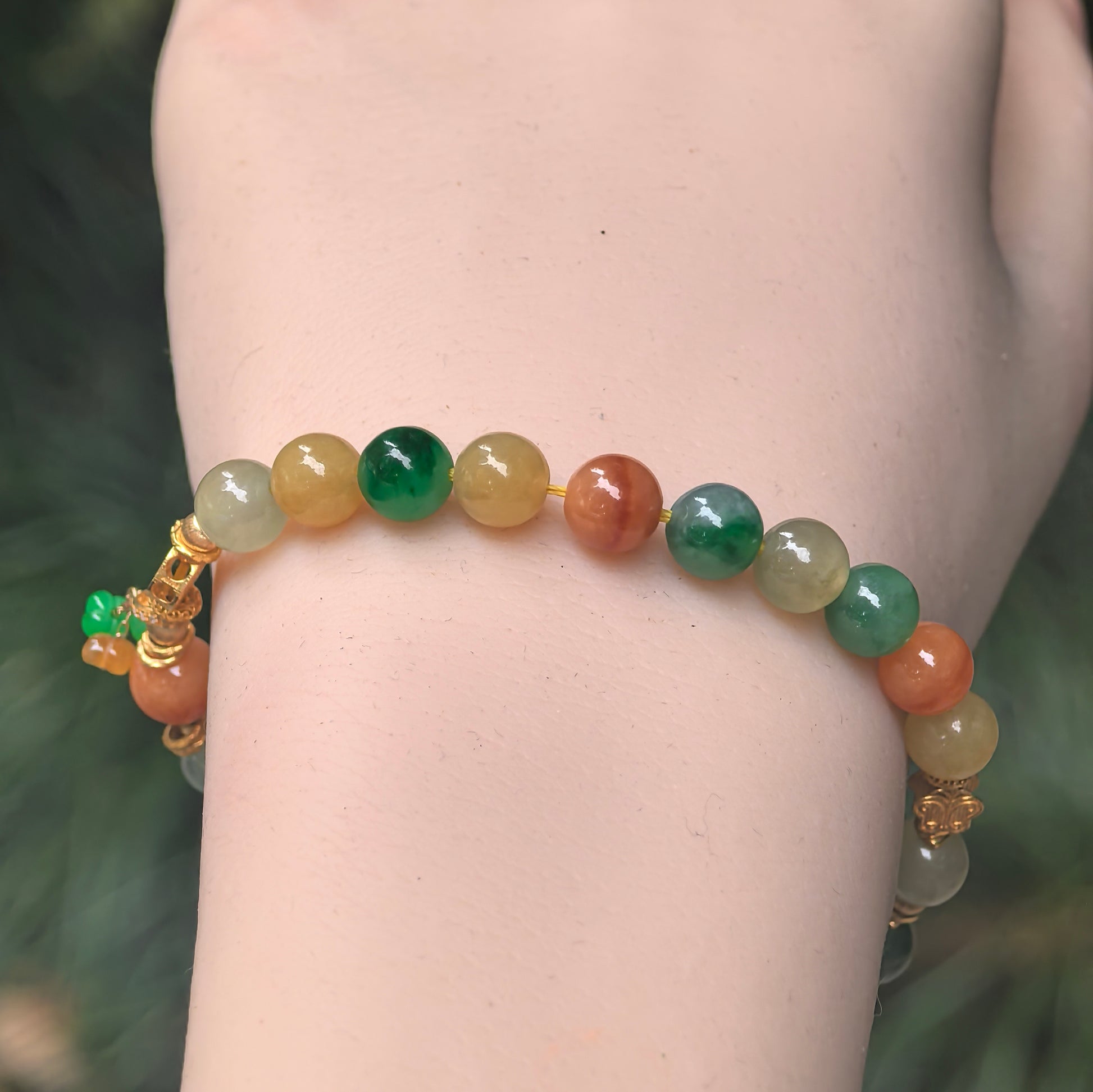 Close-up of multicolor jadeite bead bracelet showing green, yellow, and reddish tones with 18K gold details.
