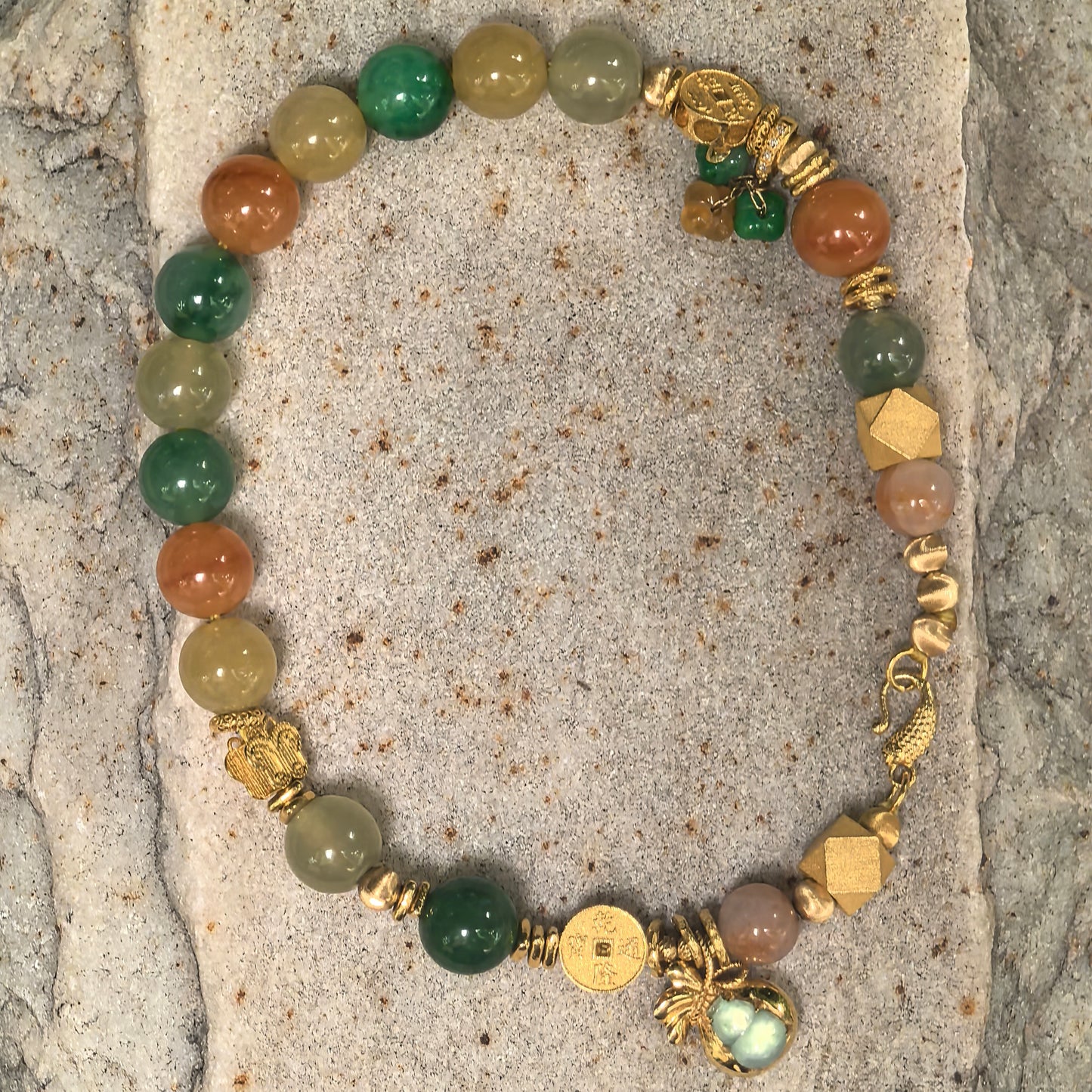 Multicolor 18K gold jadeite bracelet displayed in a round shape on stone, showing clasp and bead arrangement.
