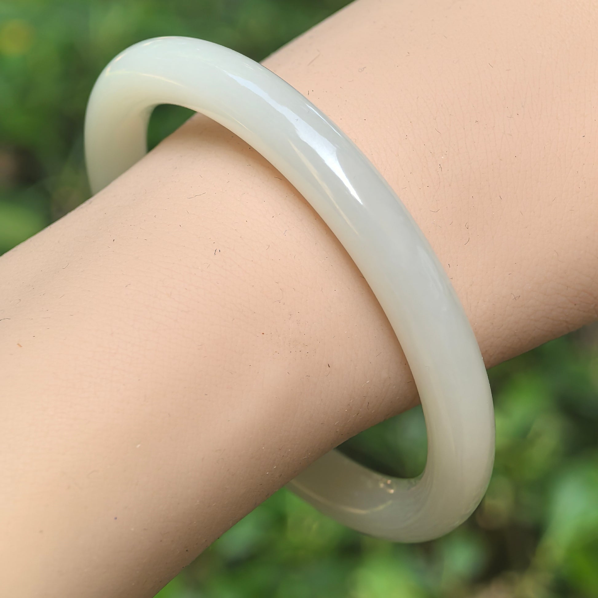 Natural Qinghai Hetian white jade slim round-bar bangle worn on the wrist with soft white color and smooth polish.
