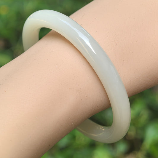 Natural Qinghai Hetian white jade slim round-bar bangle worn on the wrist with soft white color and smooth polish.
