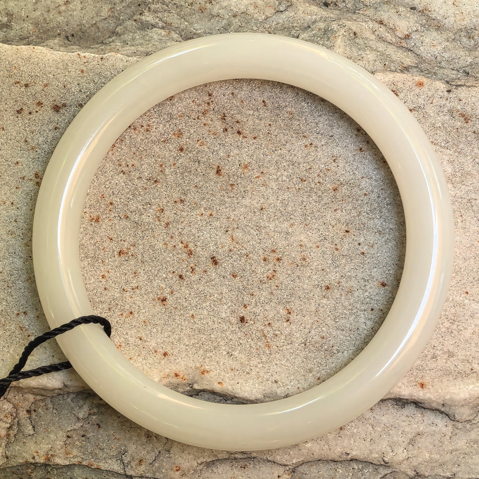 Natural Hetian white jade slim round-bar bangle displayed on stone with circular shape and soft luster.
