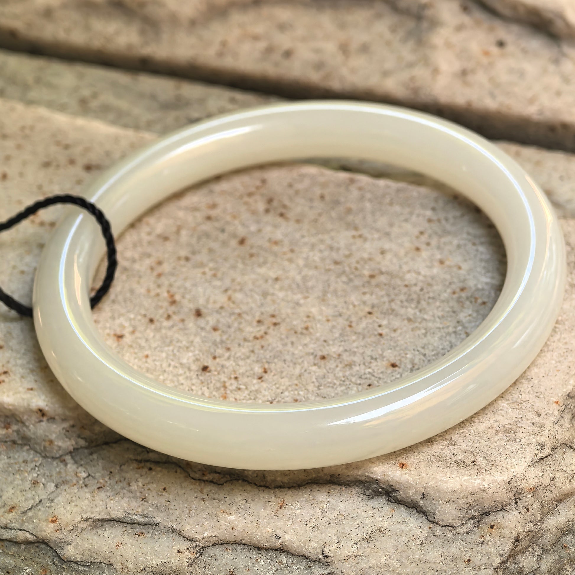 Side view of white Hetian jade bangle showing slim round-bar profile and polished finish.

