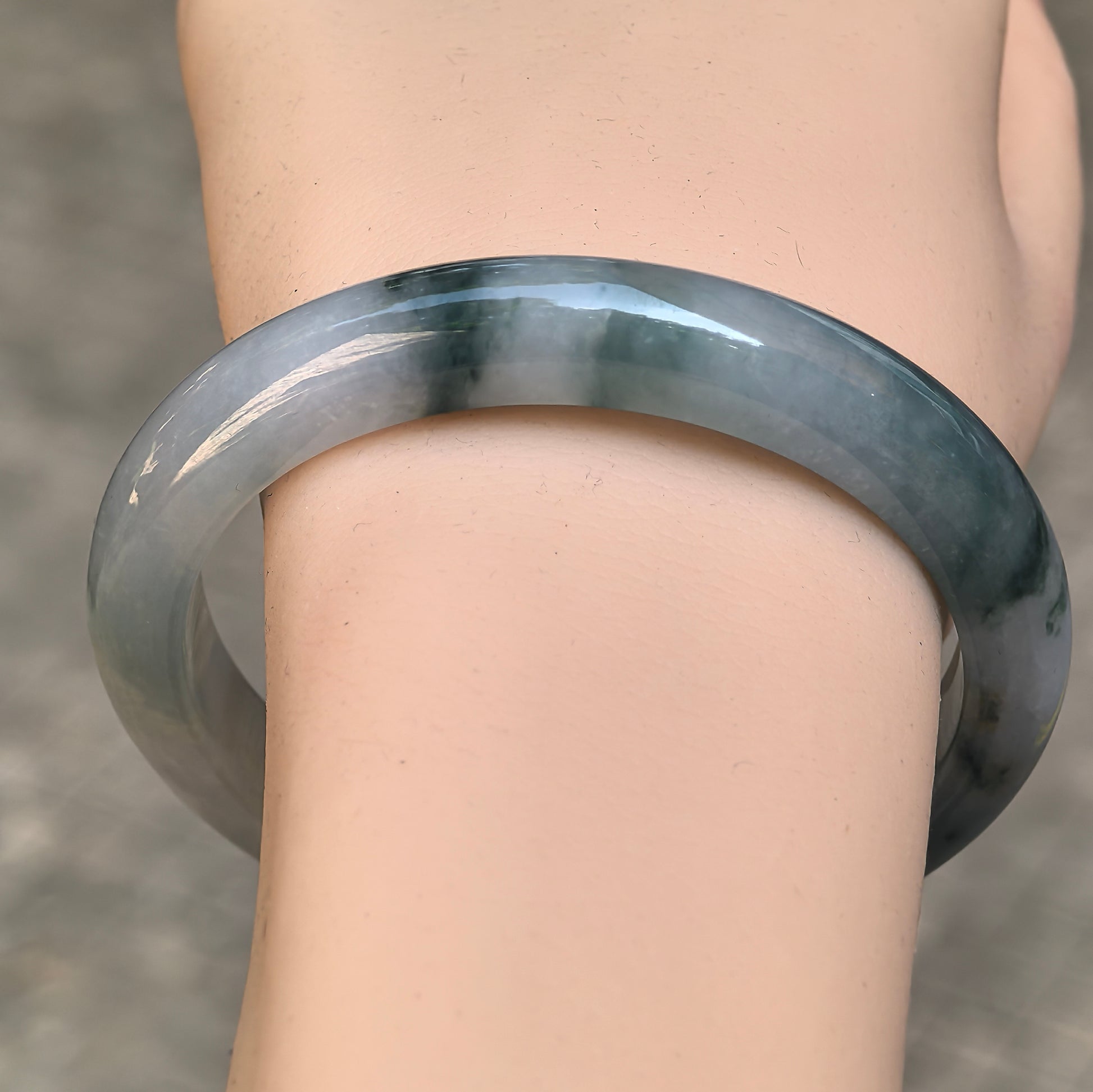 D-shape jadeite bangle with light green base and deep green floating patterns shown on wrist.
