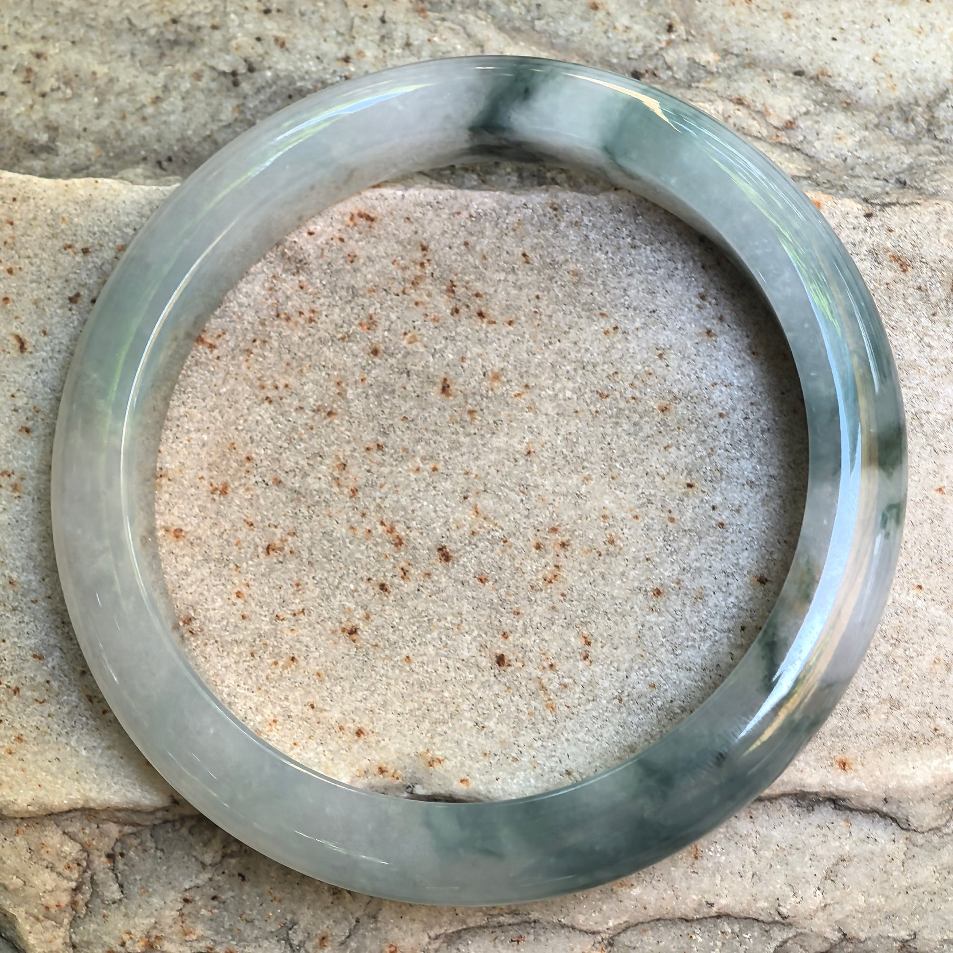 Natural Grade-A floating flower jadeite bangle displayed flat on stone background.
