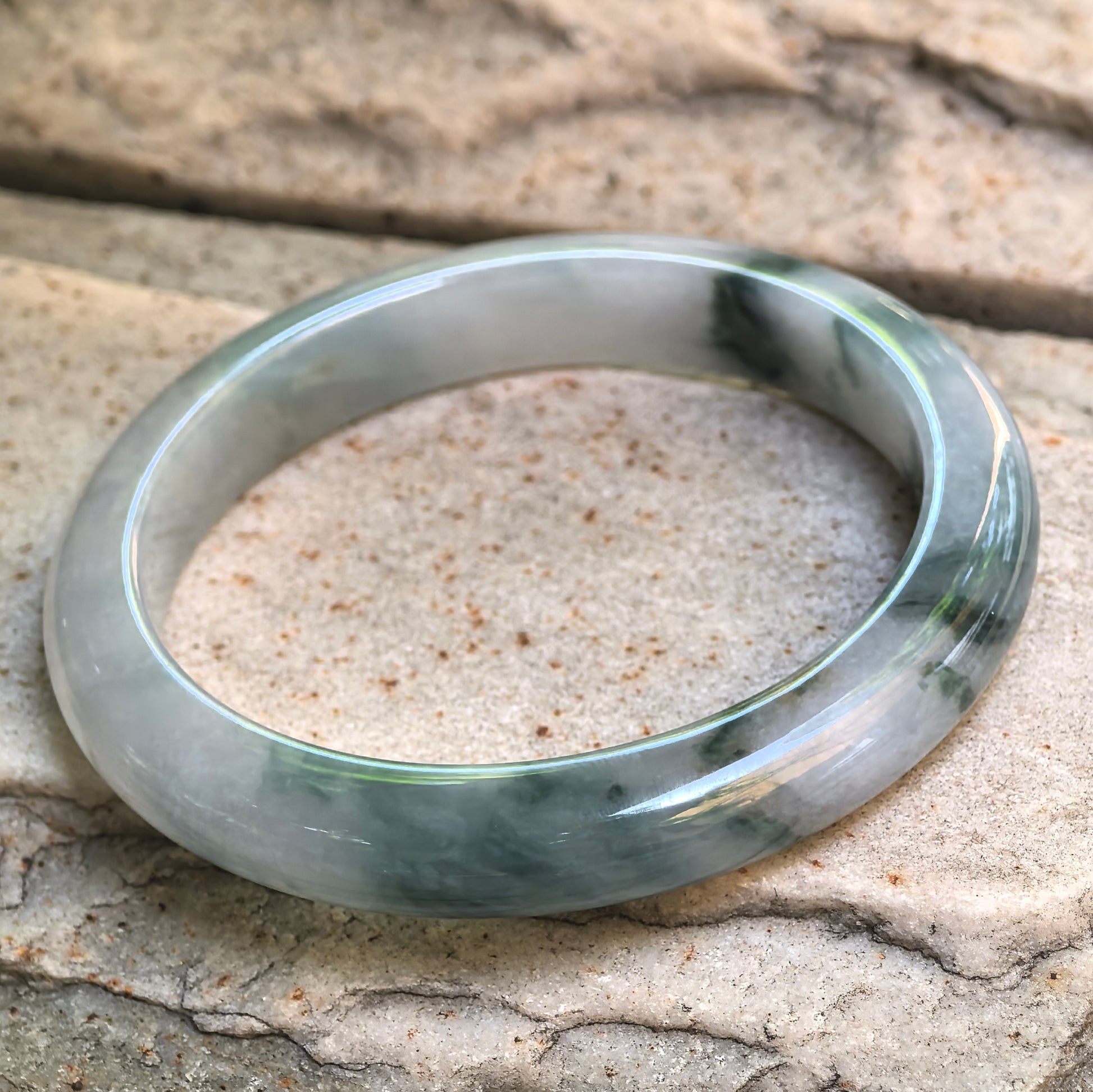 Side view of D-shape jadeite bangle with deep green floating flower areas and good translucency.
