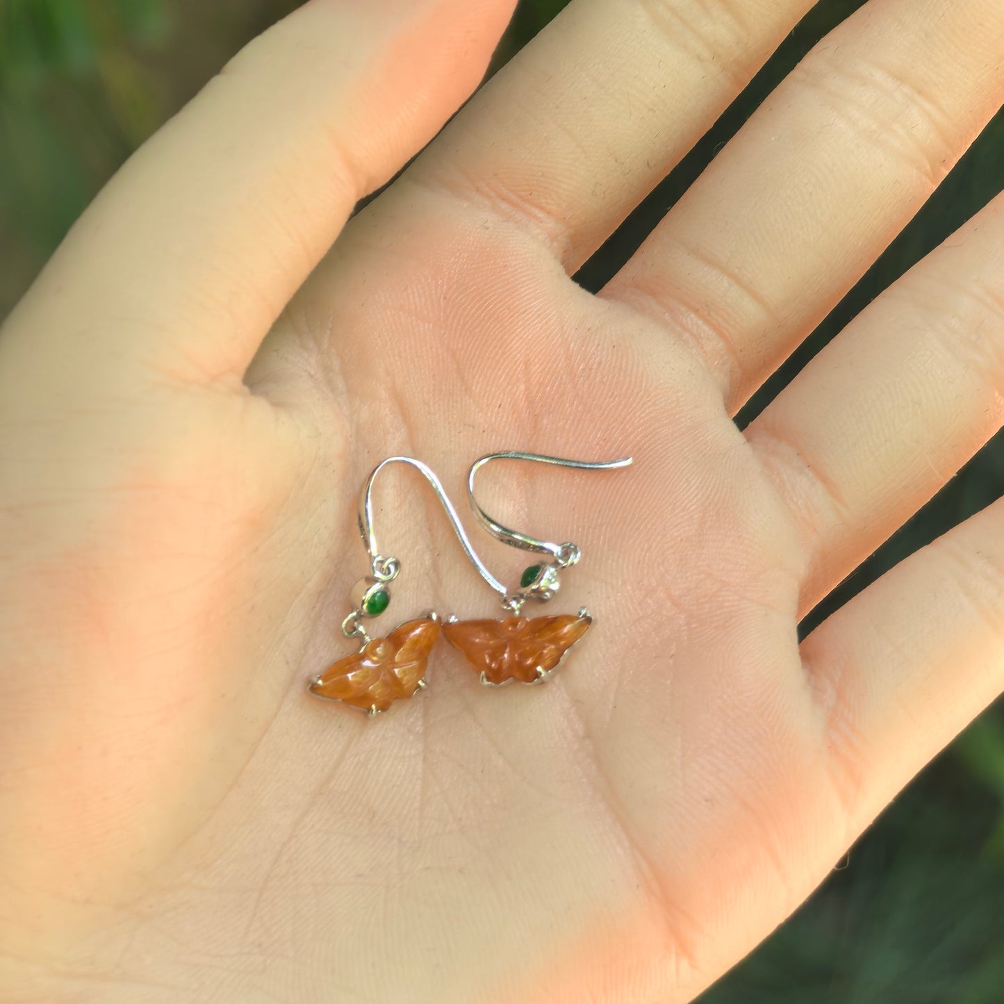Pair of 18K gold butterfly jadeite earrings with honey yellow carvings and green accents shown in hand.
