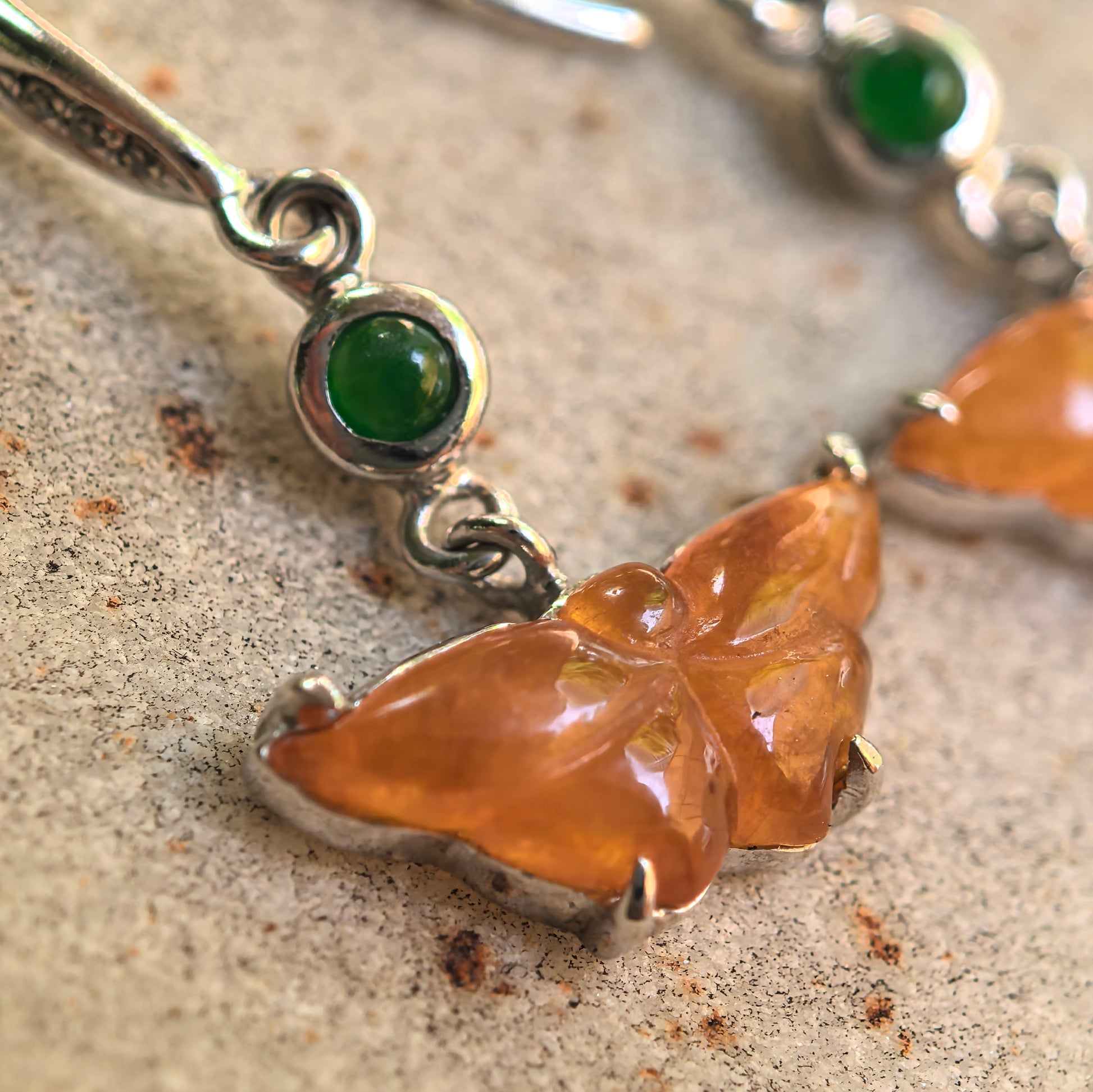 Natural Grade-A butterfly jadeite earrings displayed on stone background with green accent stones.
