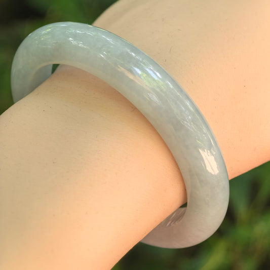 Natural Grade-A glutinous pale green D-shape jadeite bangle worn on wrist under natural light.
